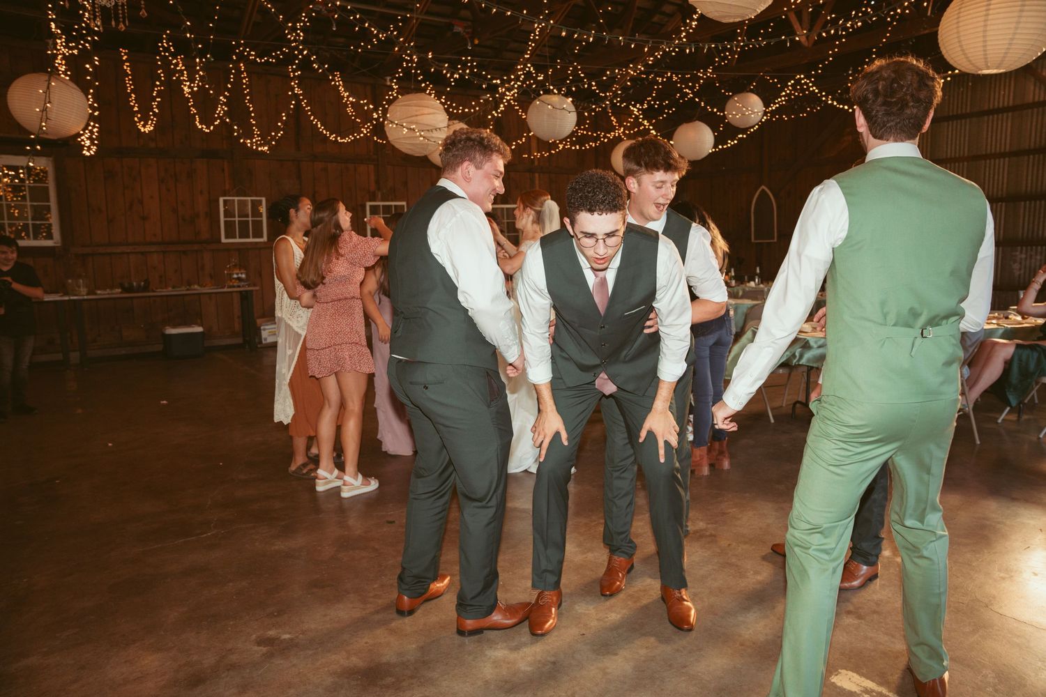 Wedding guests performing choreographed dance moves in a decorated barn venue.