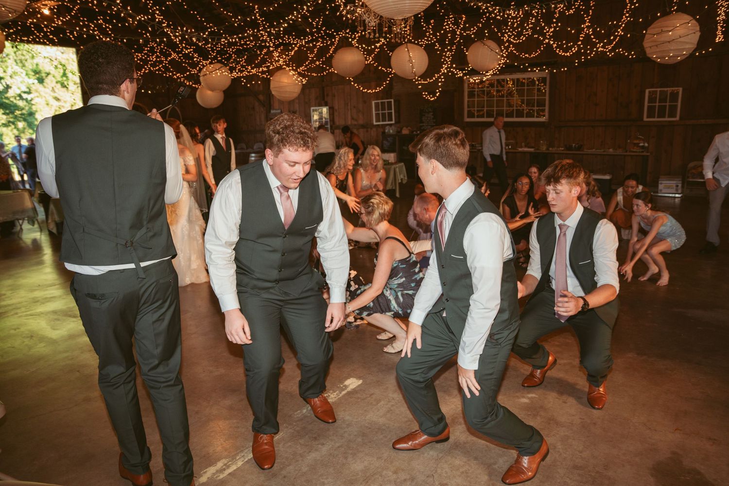 Wedding celebration with guests dancing in formal attire under romantic string light decor.