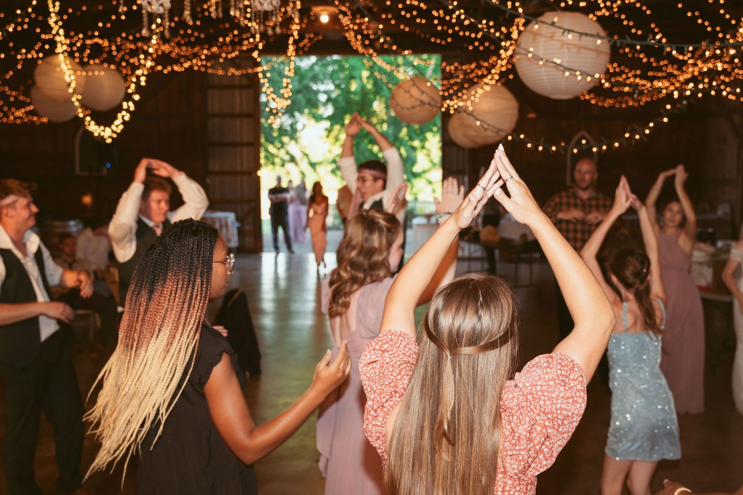 Guests dancing and celebrating at a rustic wedding reception with twinkle lights and lantern decor.