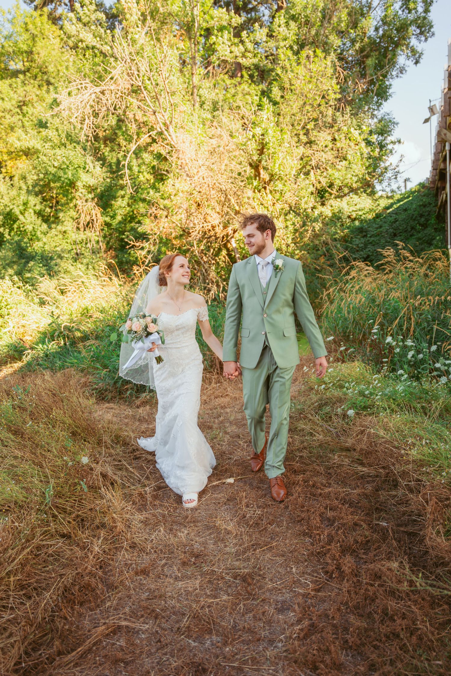 Wedding couple walking and posing playfully on a rustic dirt path surrounded by greenery.