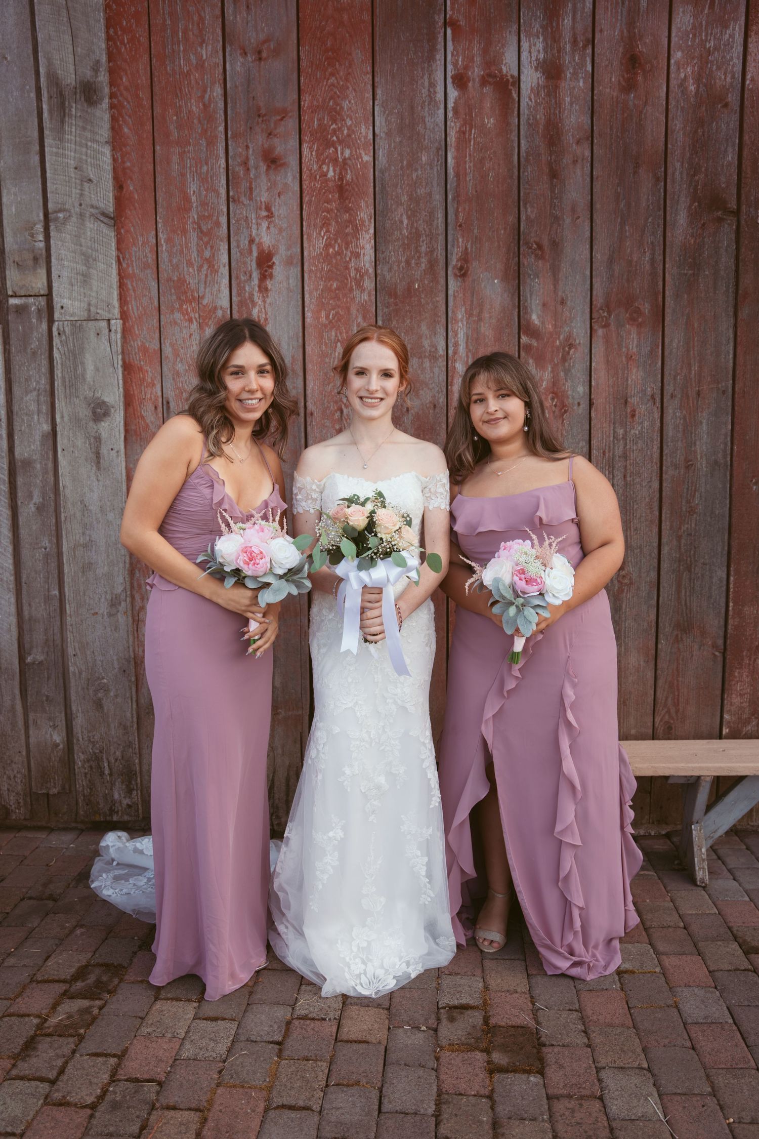 Wedding group photo featuring bridesmaids in mauve dresses and bride in white lace gown.