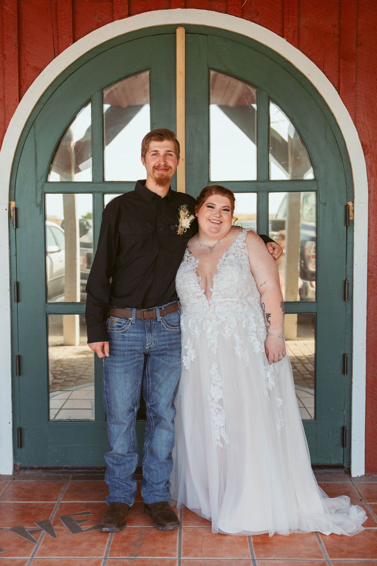 Wedding party poses casually in front of green arched doorways and red building exterior.