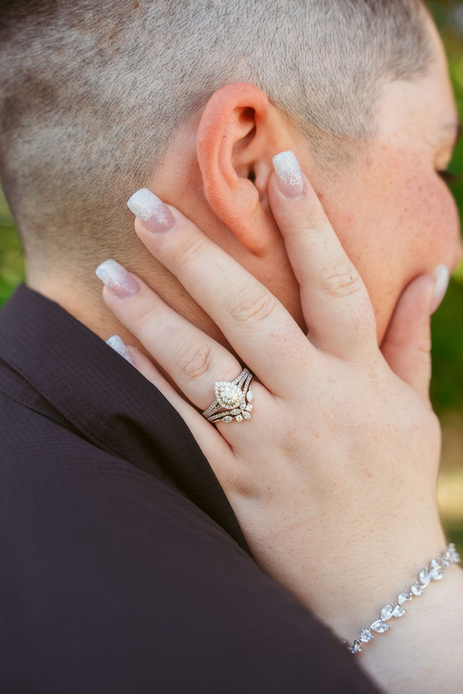 A hand with French manicured nails and a diamond engagement ring touches the back of someone's head.