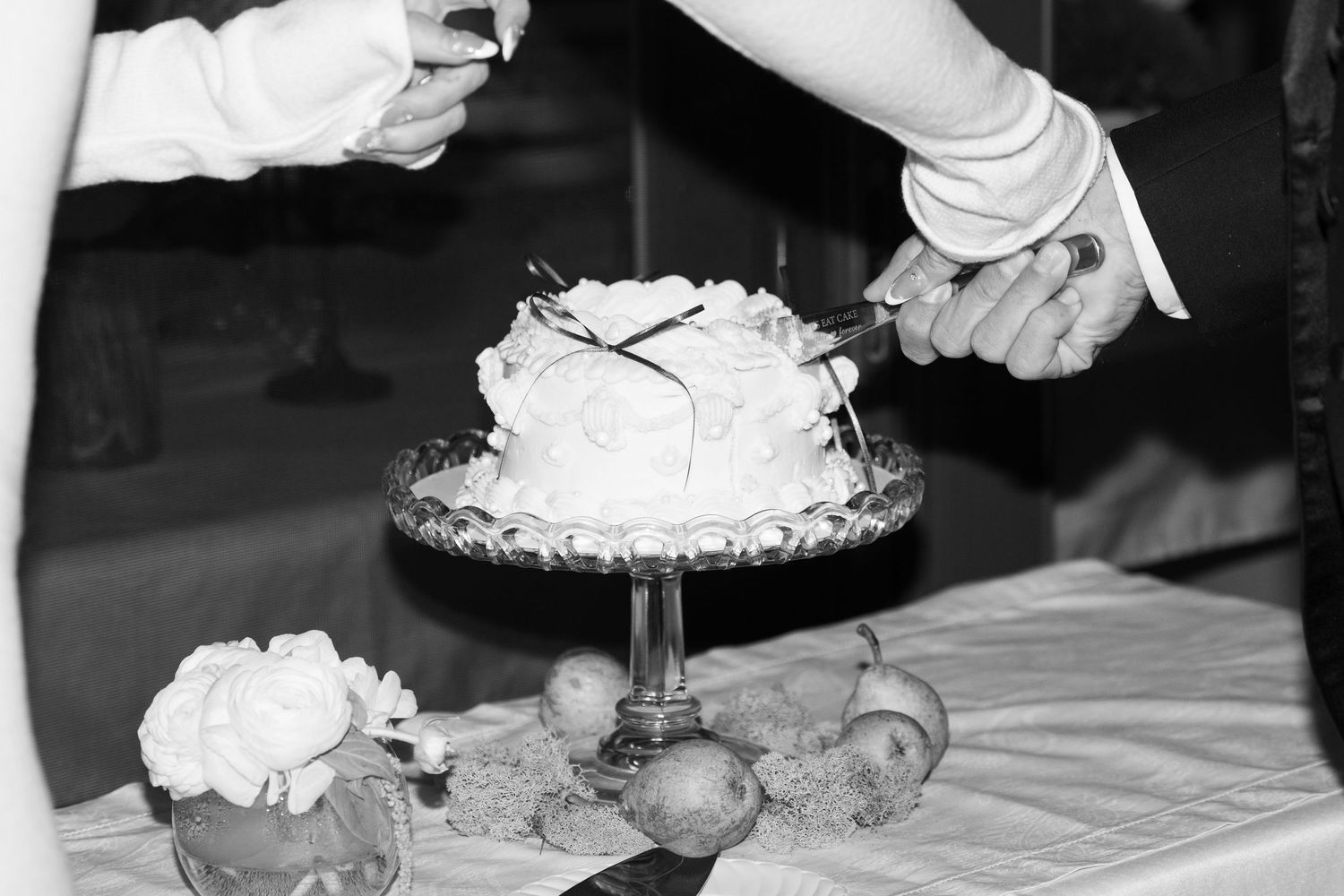 Close-up of hands cutting into an elegant white wedding cake at a reception.