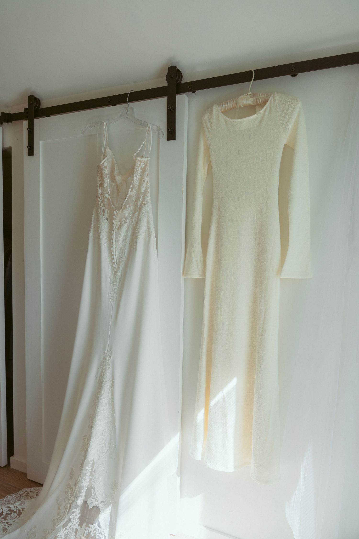 Collection of white wedding dresses hanging on a wooden rod against a white wall.