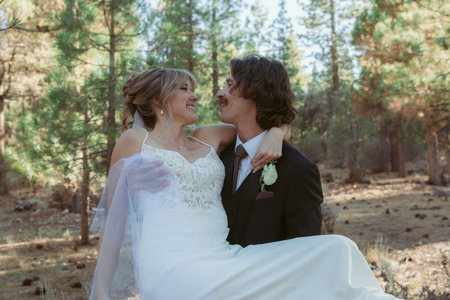 A romantic wedding photoshoot in a sunlit forest with pine trees creating a natural backdrop.