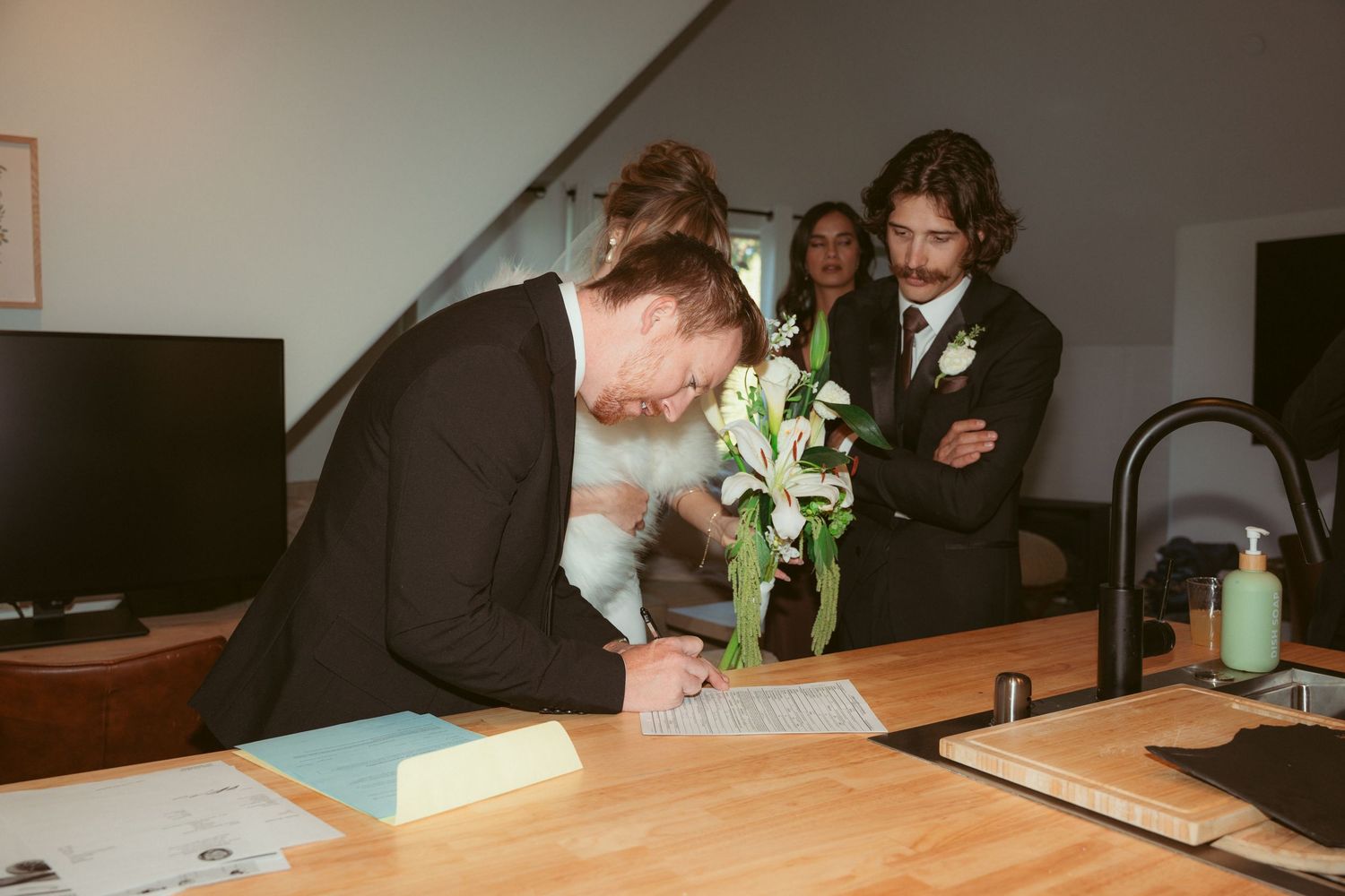 Wedding guests signing papers at a wooden table during a formal event.