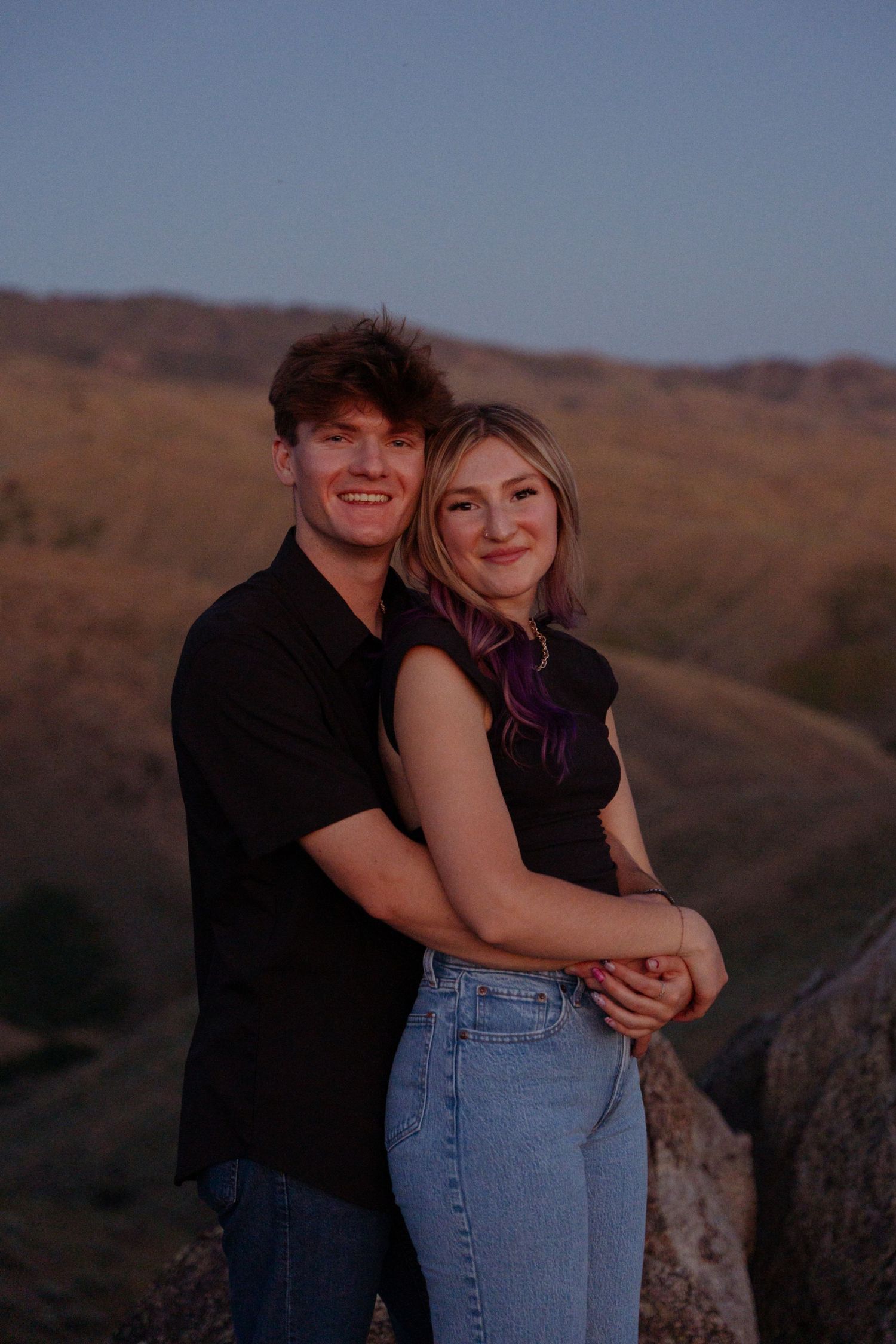 Couple poses for sunset portrait on rocky mountain overlook.