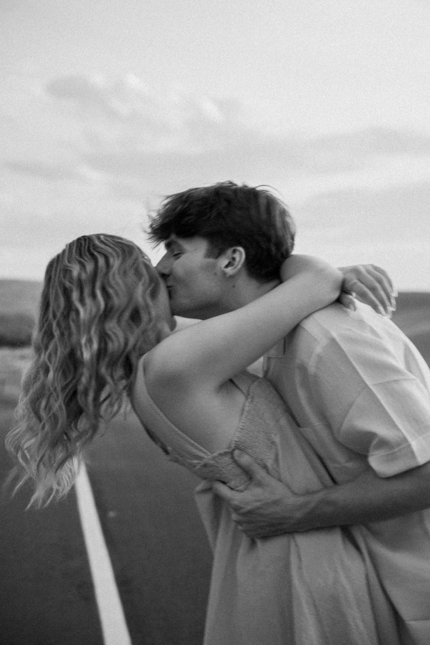 Black and white photo of a couple in a passionate embrace on a remote road.