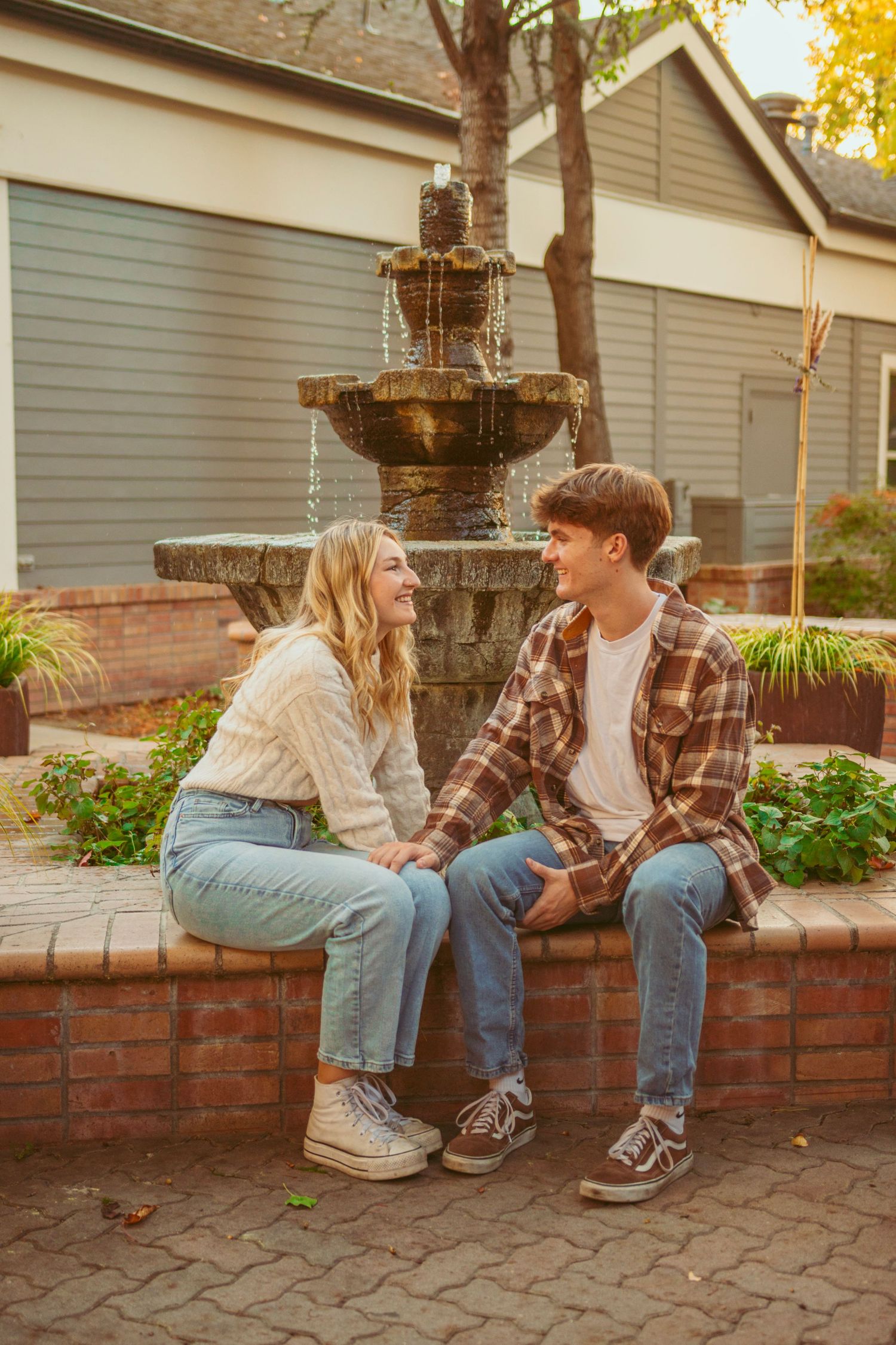 A couple sits by a decorative fountain surrounded by autumn foliage.