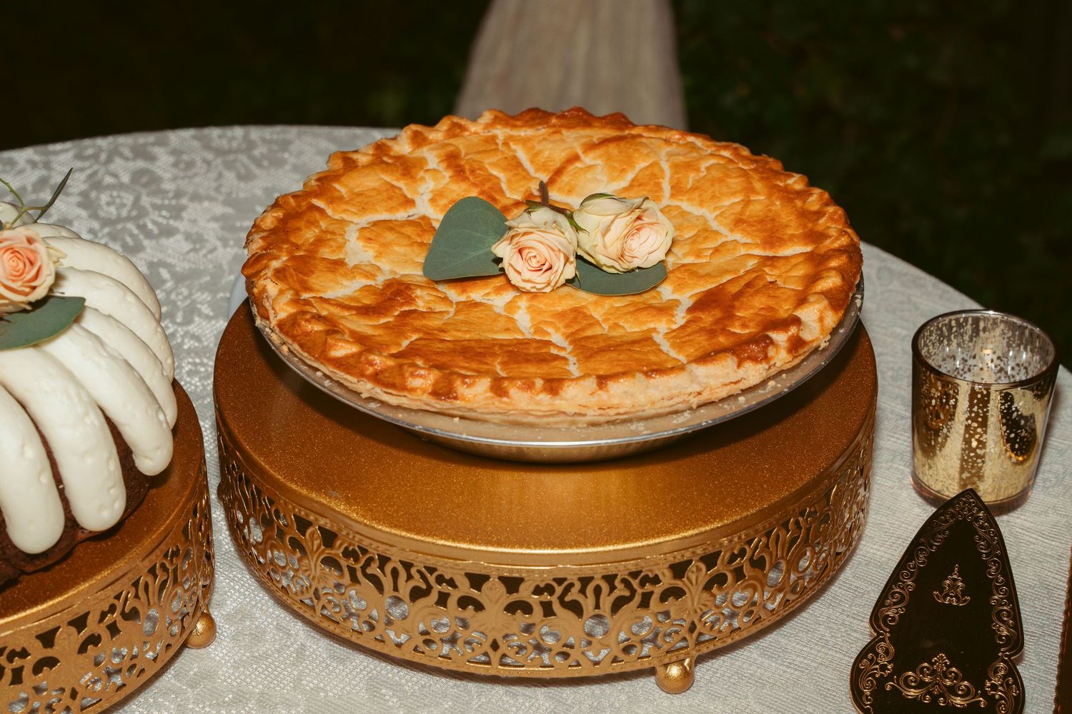 Elegant pie with decorative lattice crust displayed on ornate gold cake stand with candle holders.