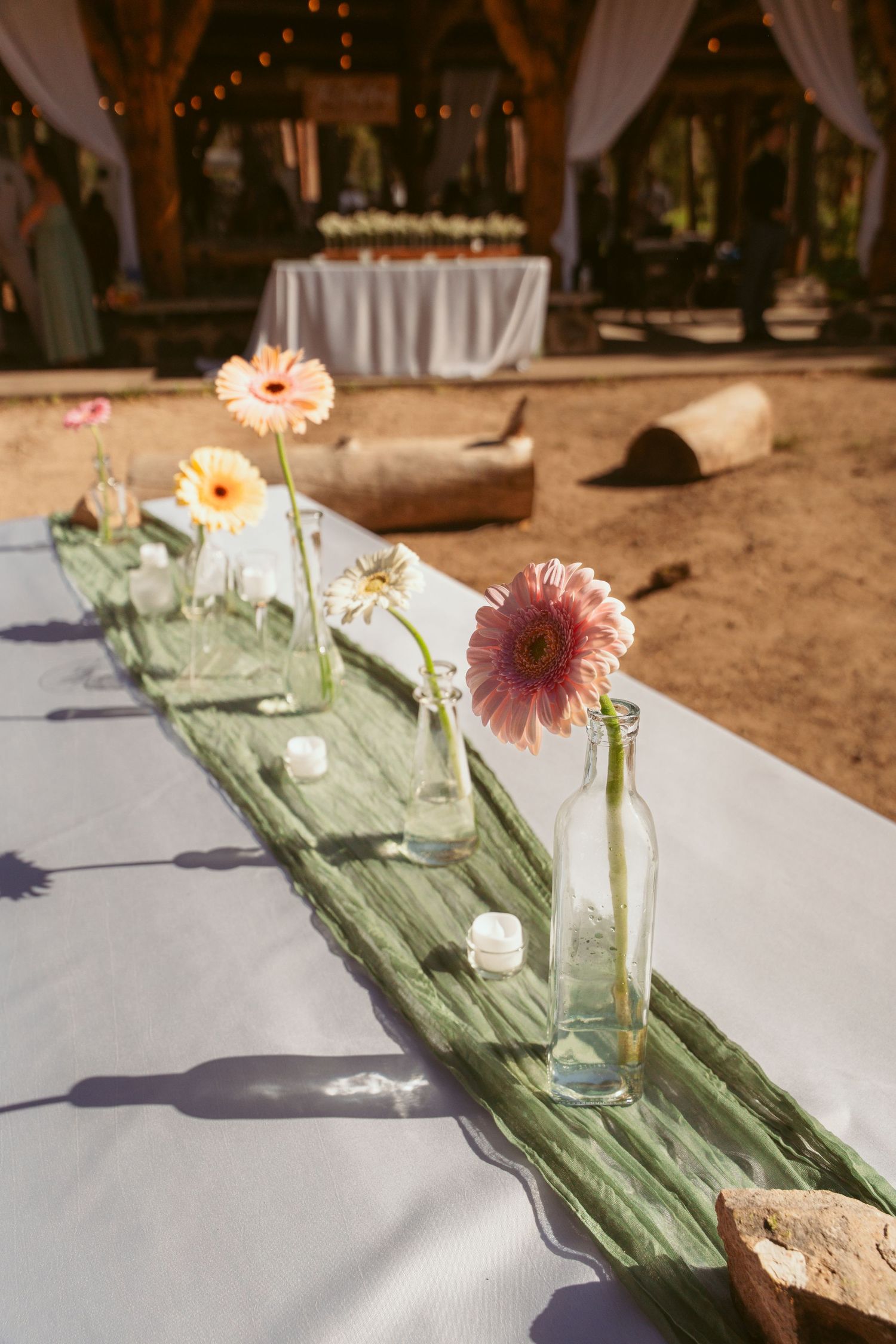 White tablecloths decorated with green runners and pink gerbera daisies for an outdoor event setting.