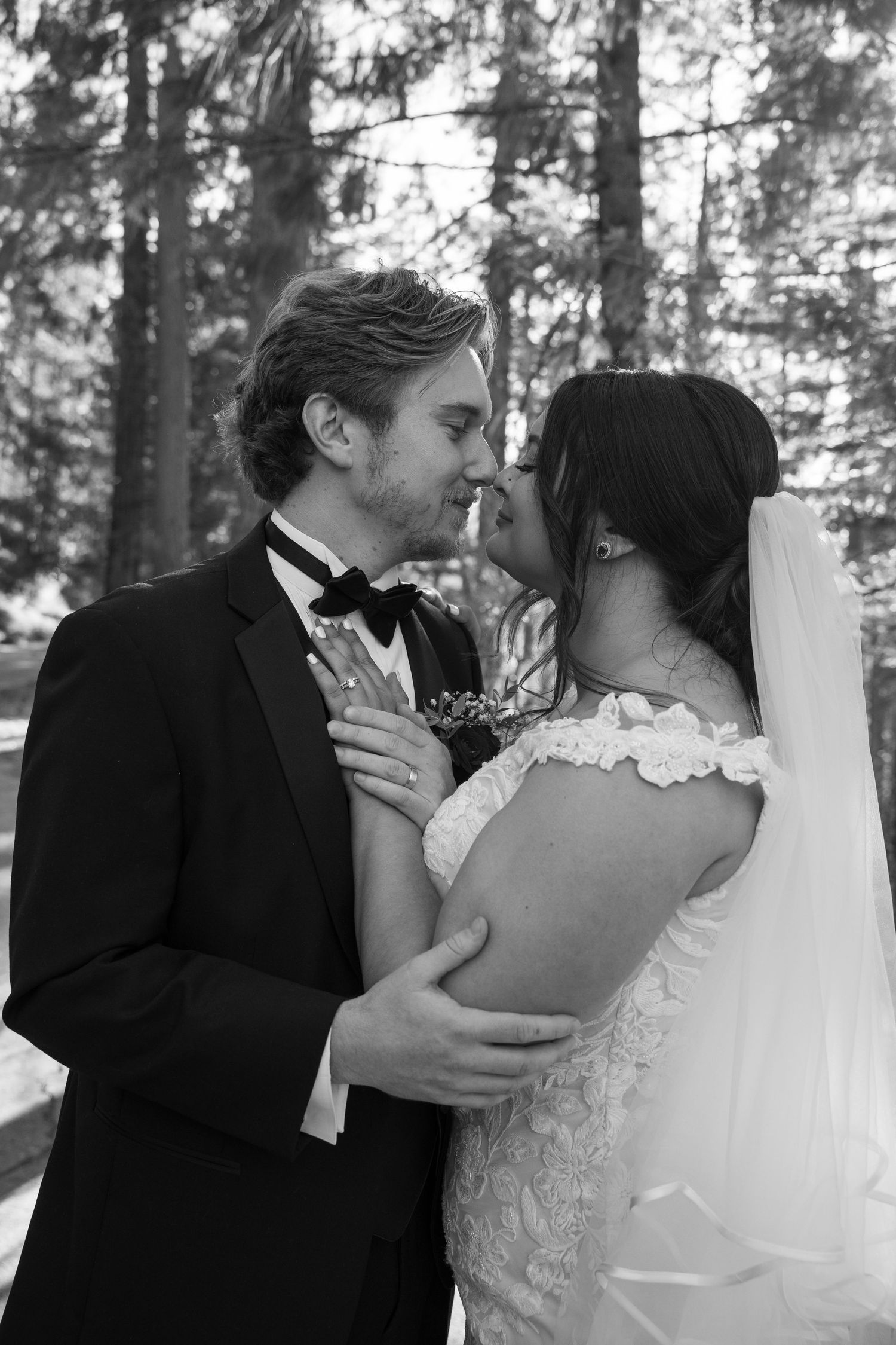 An intimate moment between newlyweds in formal attire against a forest backdrop.