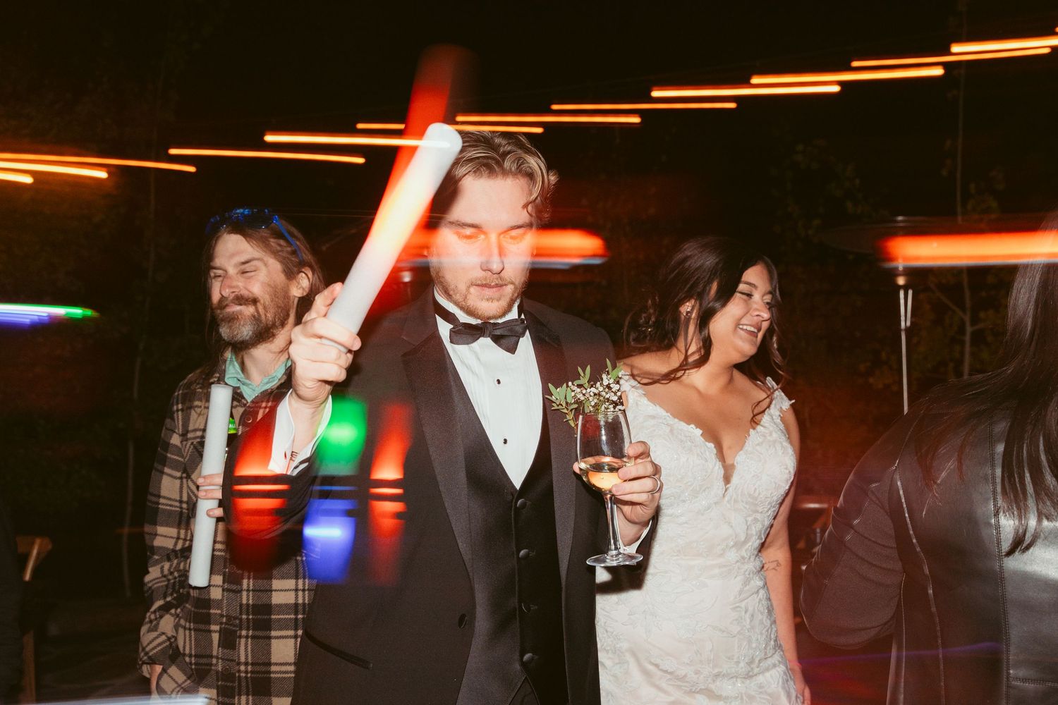 Wedding guests dancing and celebrating with glowing LED accessories at night.