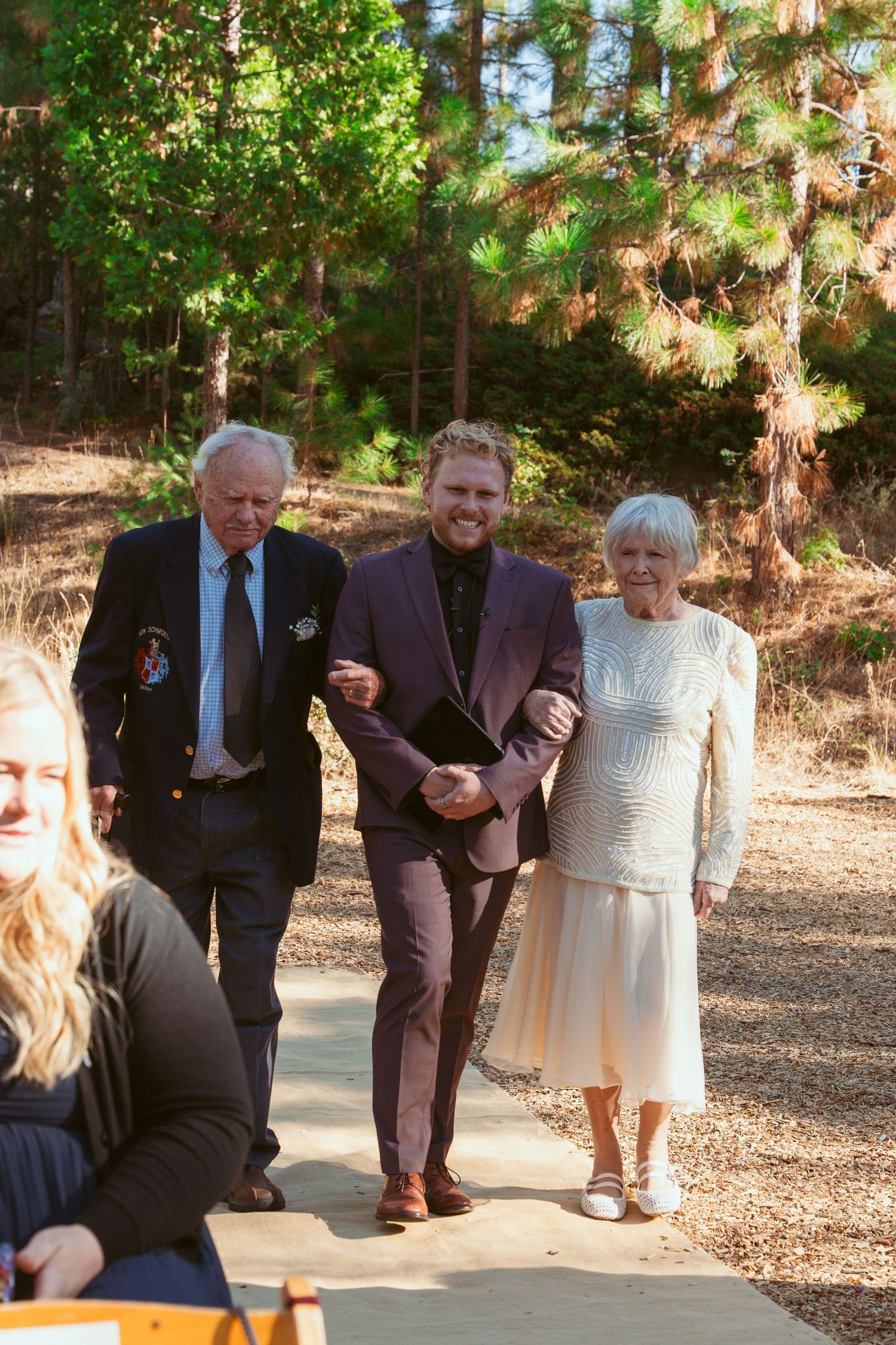 Three wedding guests walking down a wooded path at an outdoor ceremony venue.
