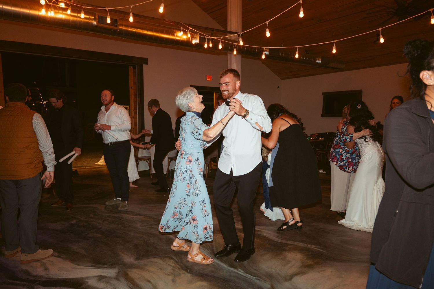 Couples slow dancing at a wedding reception under warm string lights.