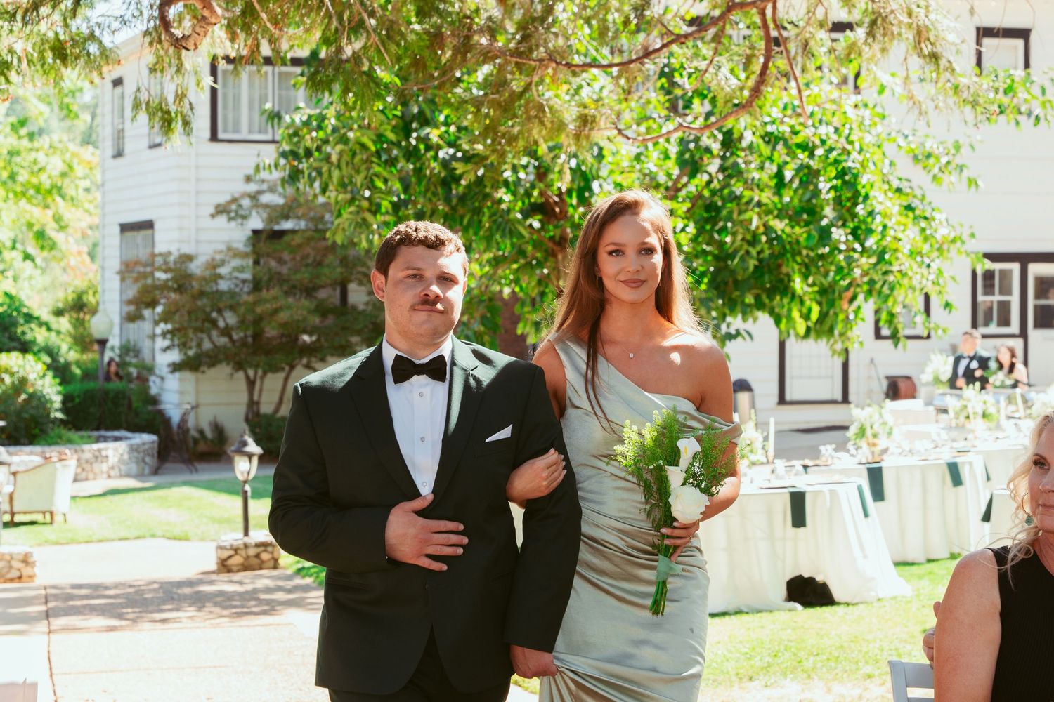 Wedding party gathering in a sunlit garden venue with elegant outdoor decor and greenery.