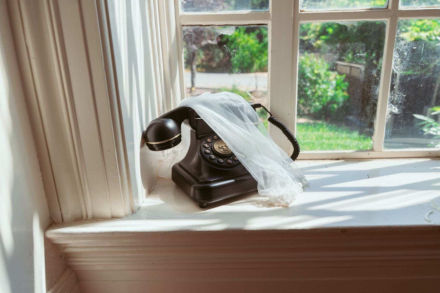 Vintage telephone displayed on windowsill with natural light streaming through white curtains.