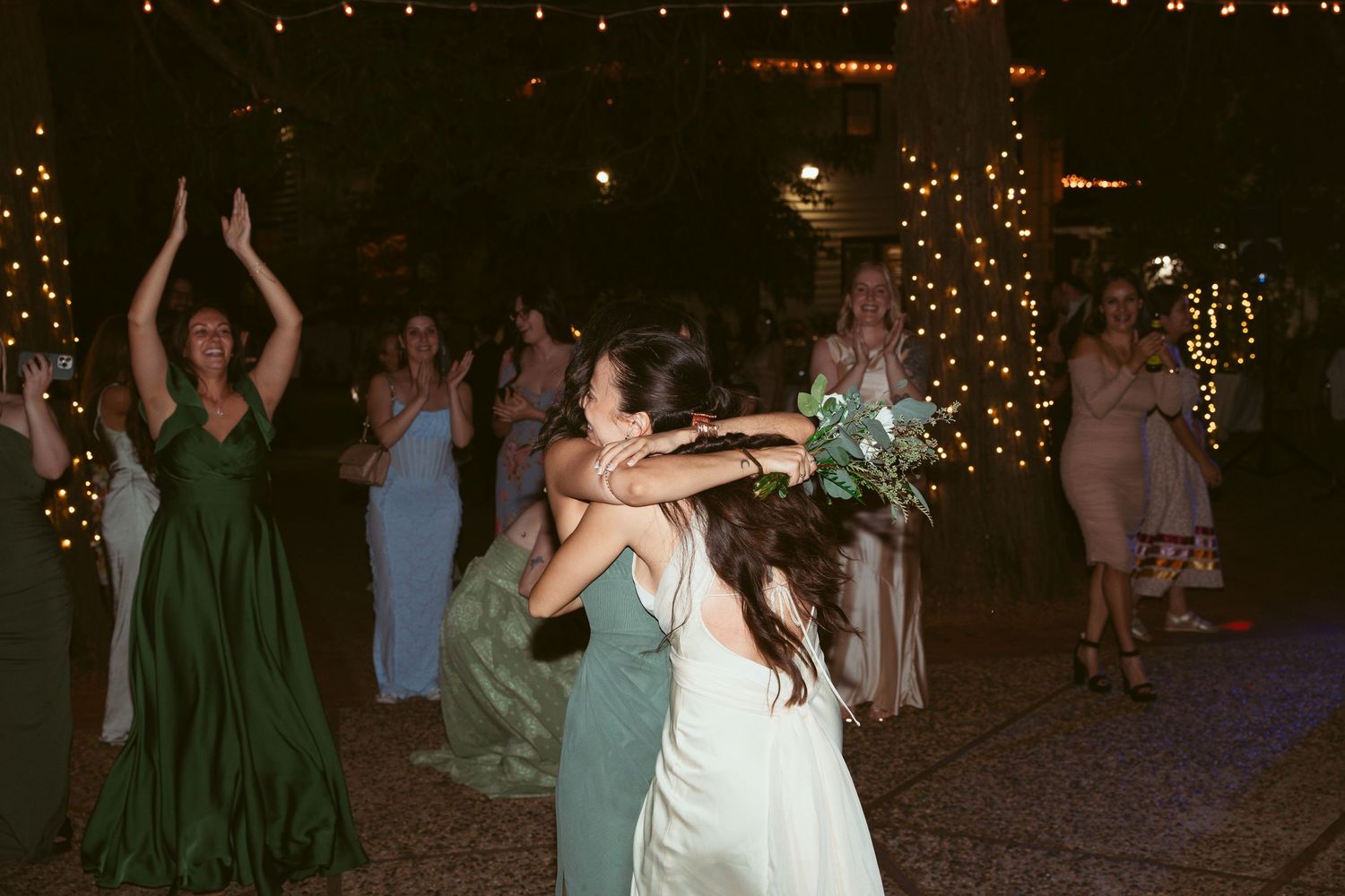 Outdoor wedding reception with guests dancing beneath strands of glowing string lights.