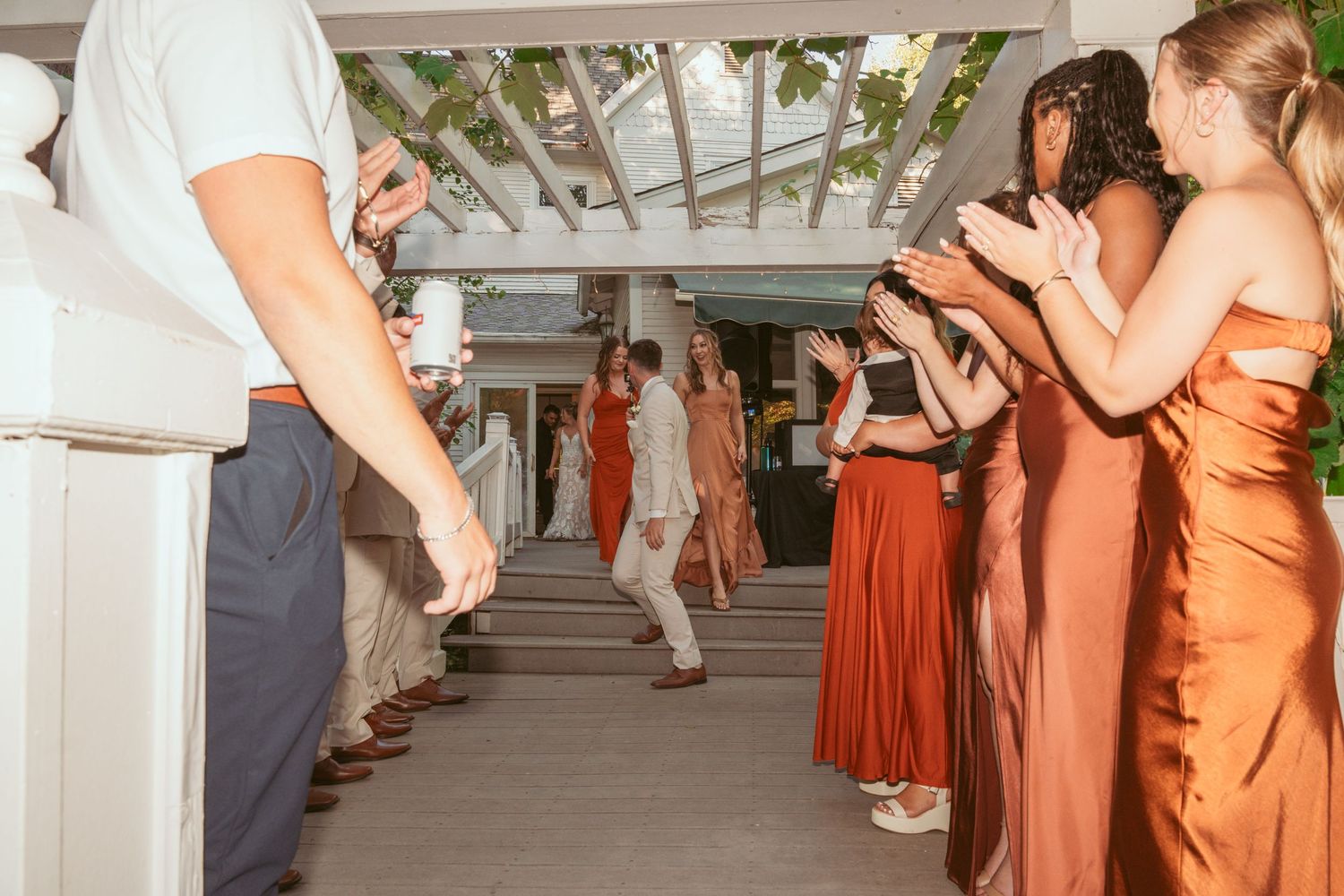 Wedding guests dance and celebrate on an outdoor patio with white pillars and warm lighting.