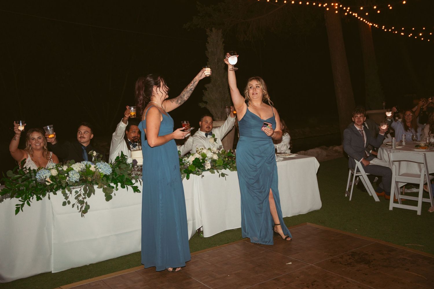Party guests dance and mingle under glowing string lights at an outdoor evening celebration.