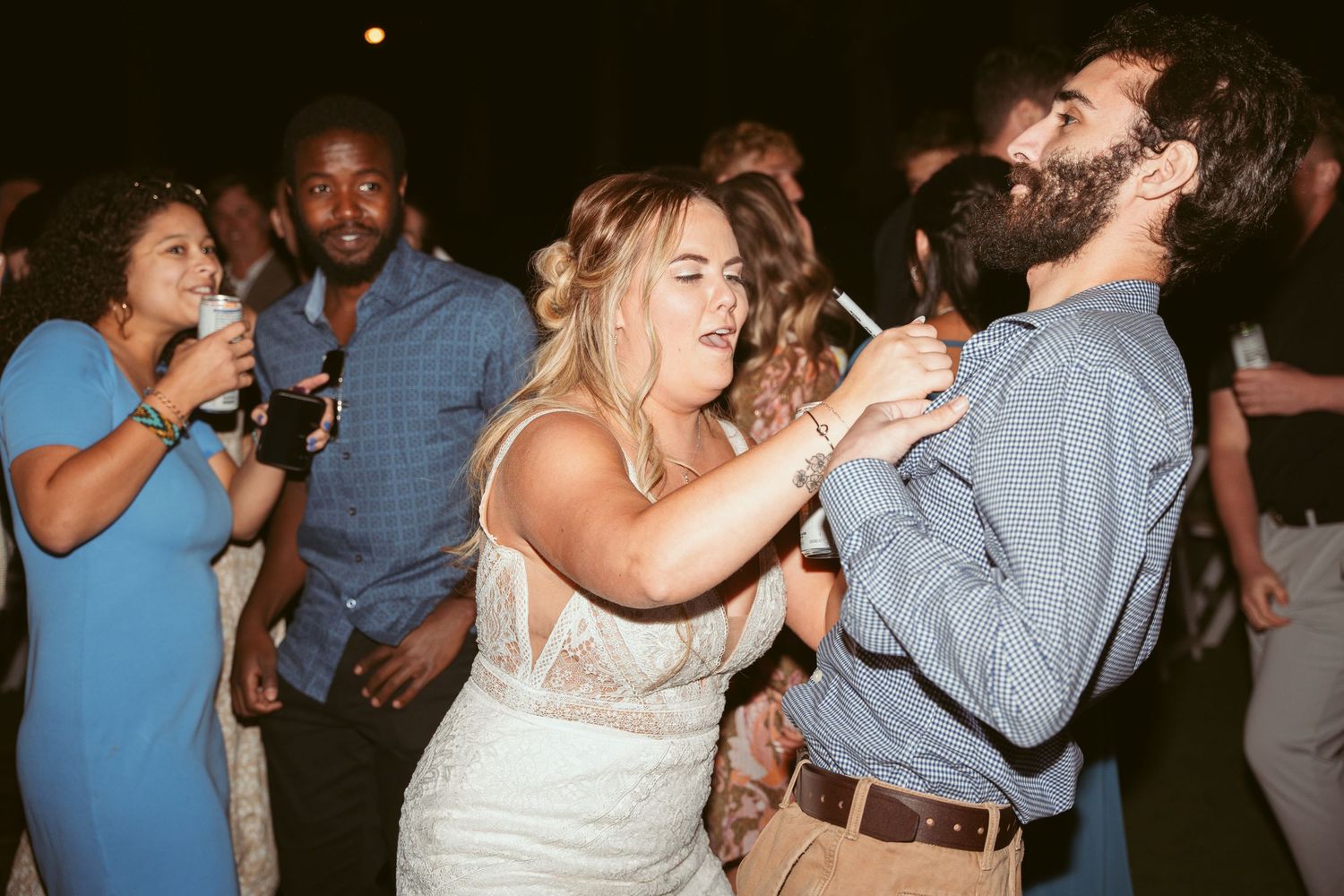 Lively dance floor scene at an outdoor wedding reception with guests enjoying themselves under string lights.