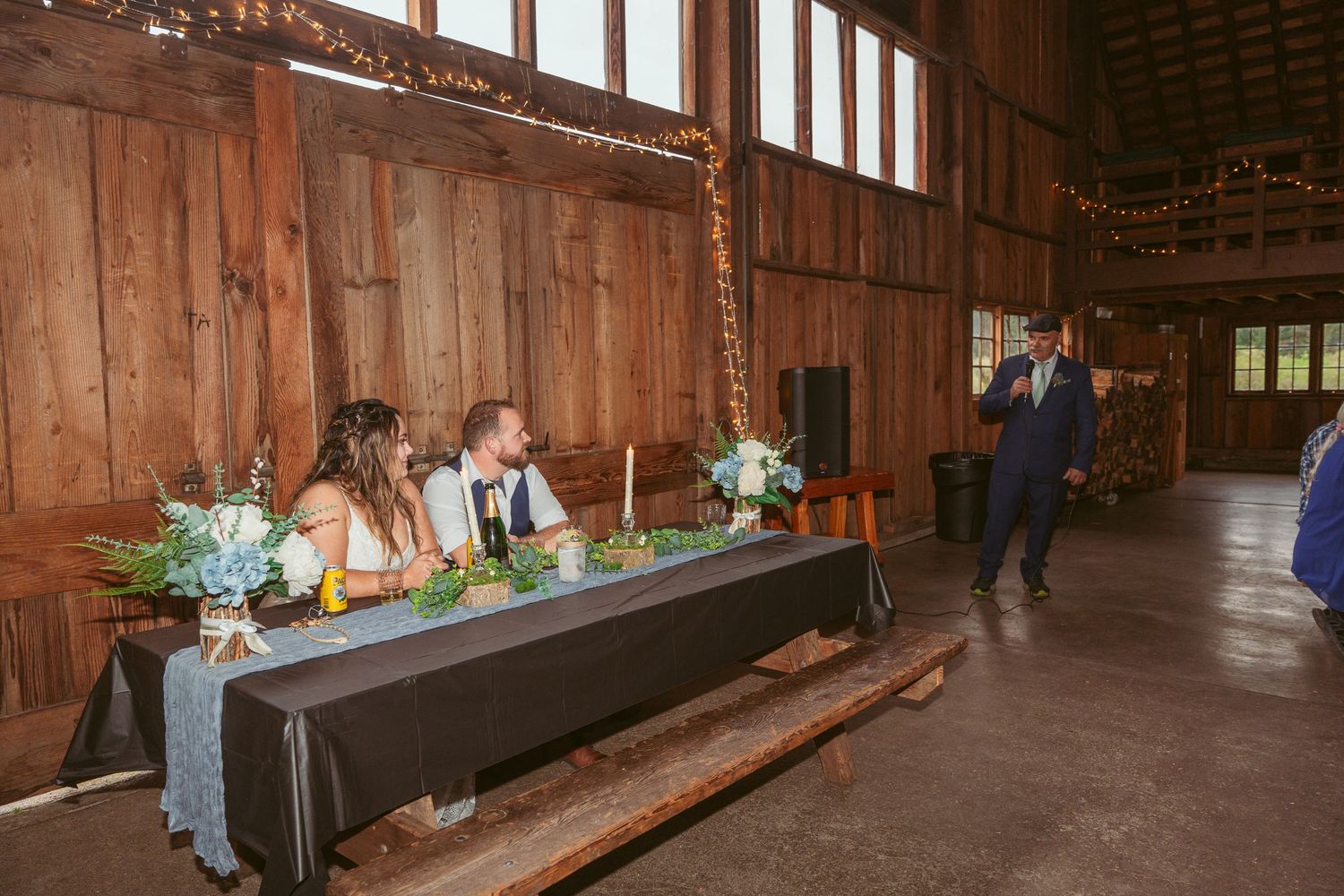 Long tables set up for wedding reception inside rustic wooden barn with natural light.