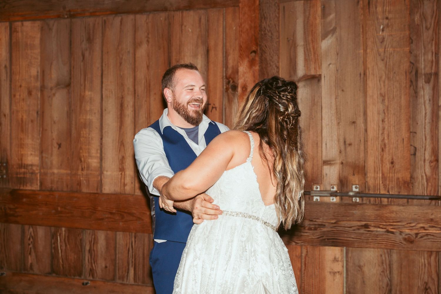 A couple shares a dance moment in a rustic barn setting with wooden walls.