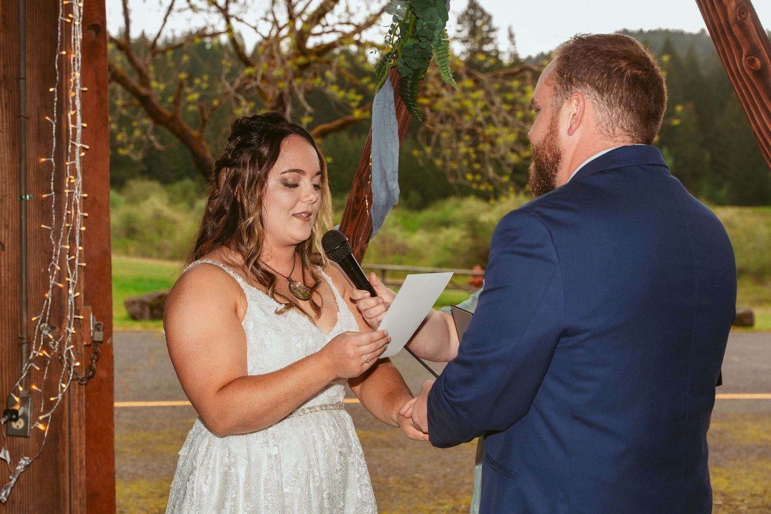 Couple sharing intimate moment during barn wedding ceremony with string lights overhead.