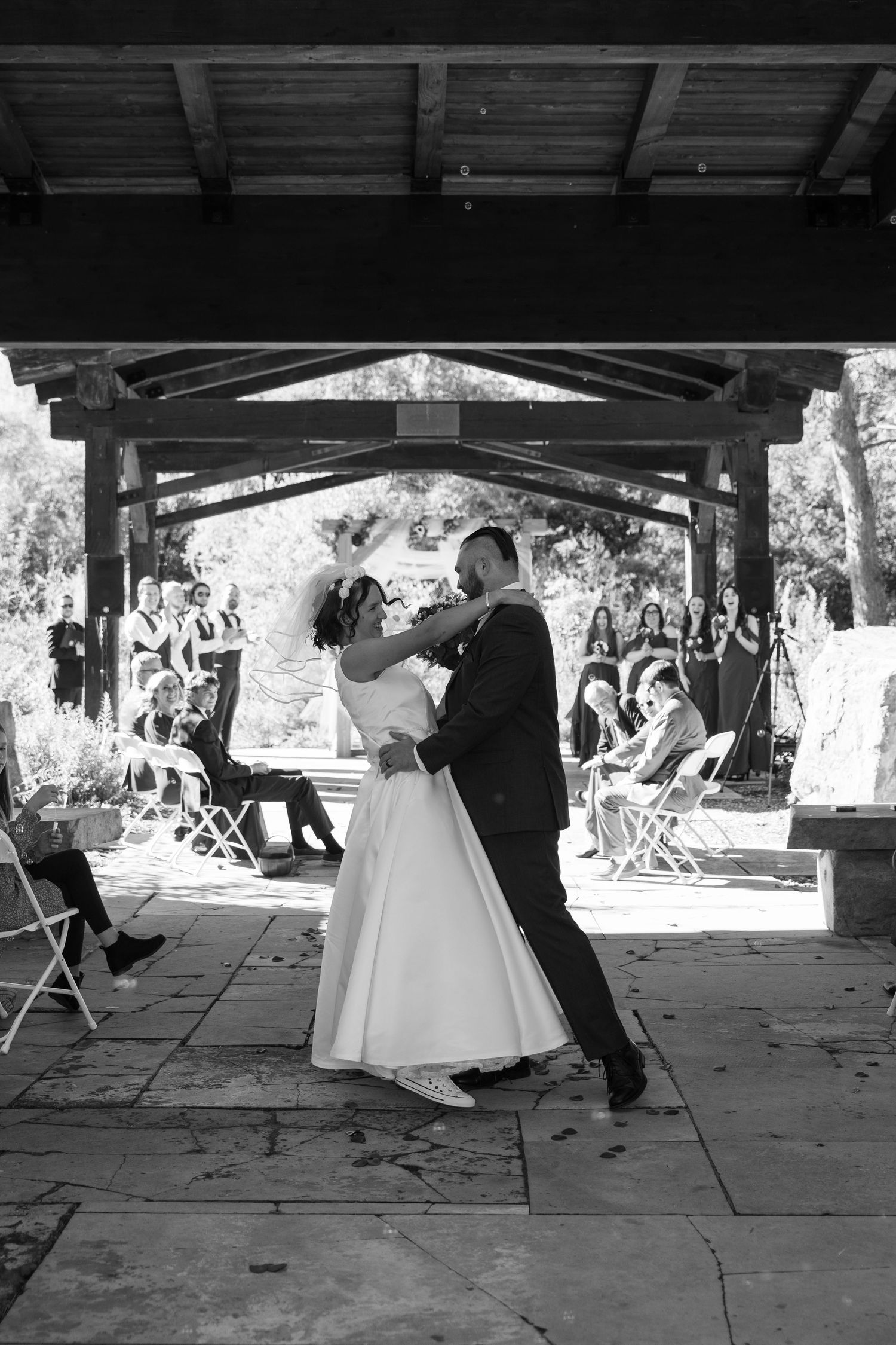 Black and white panoramic shot of a wedding ceremony under a stone pavilion with guests.