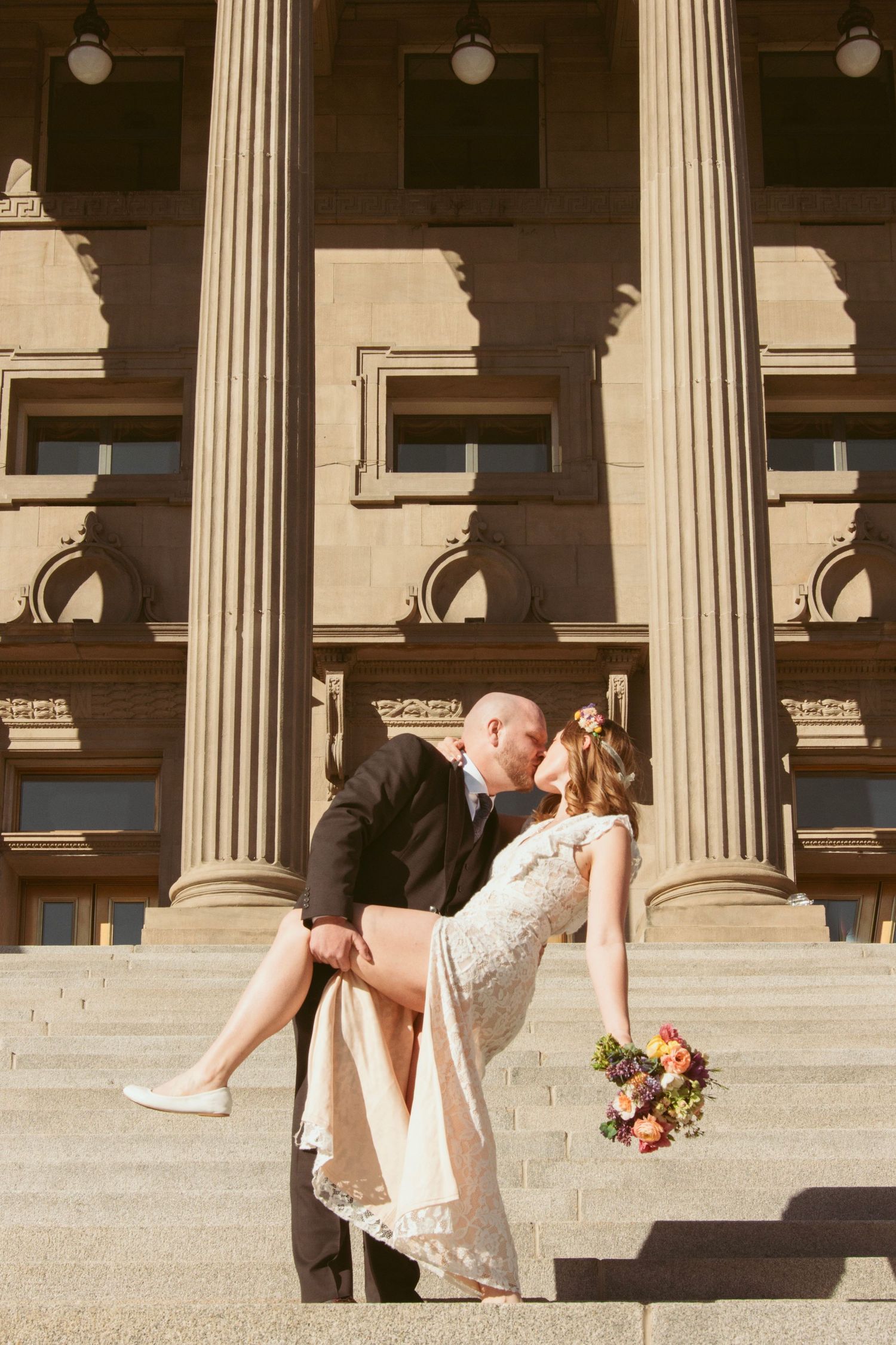 Wedding couple poses dramatically on grand stone steps with classical columns.