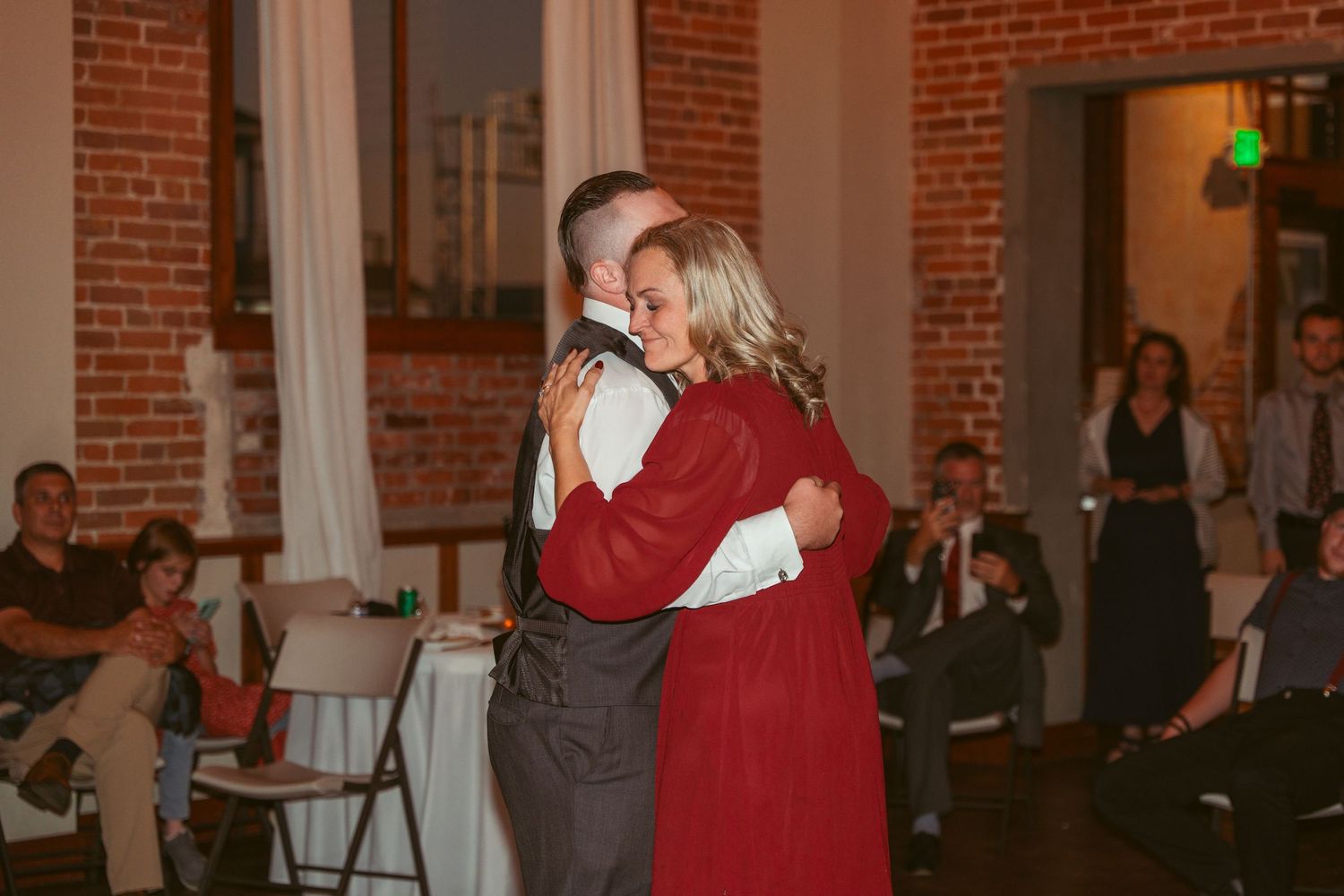 Wedding guests dancing in a warmly lit brick reception hall with decorative string lights.