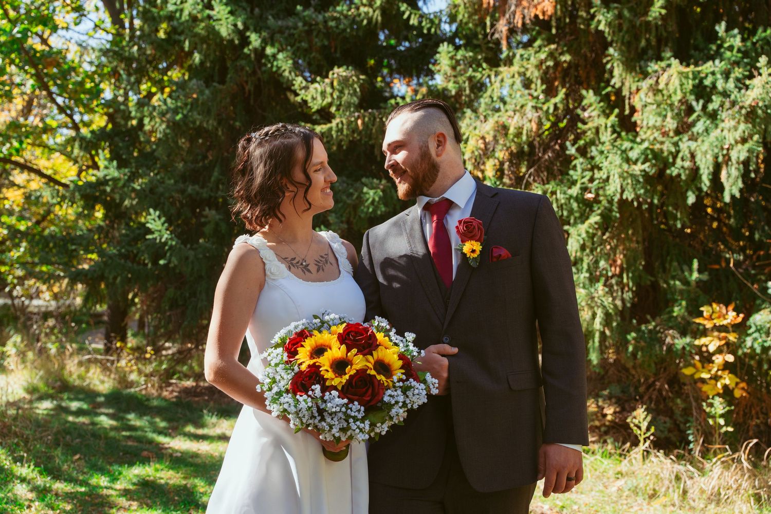 Outdoor wedding couple poses in autumn garden with sunflower bouquet and formal attire.