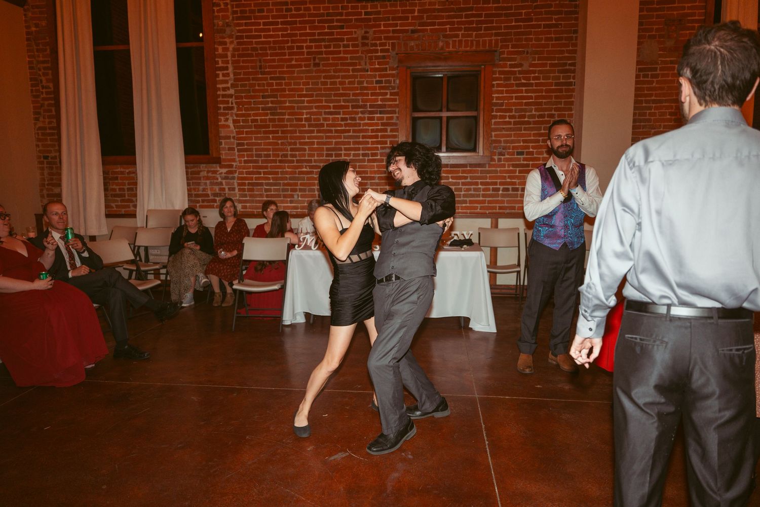 Dancing couples enjoying themselves on a wooden floor in an industrial-style venue with brick walls.