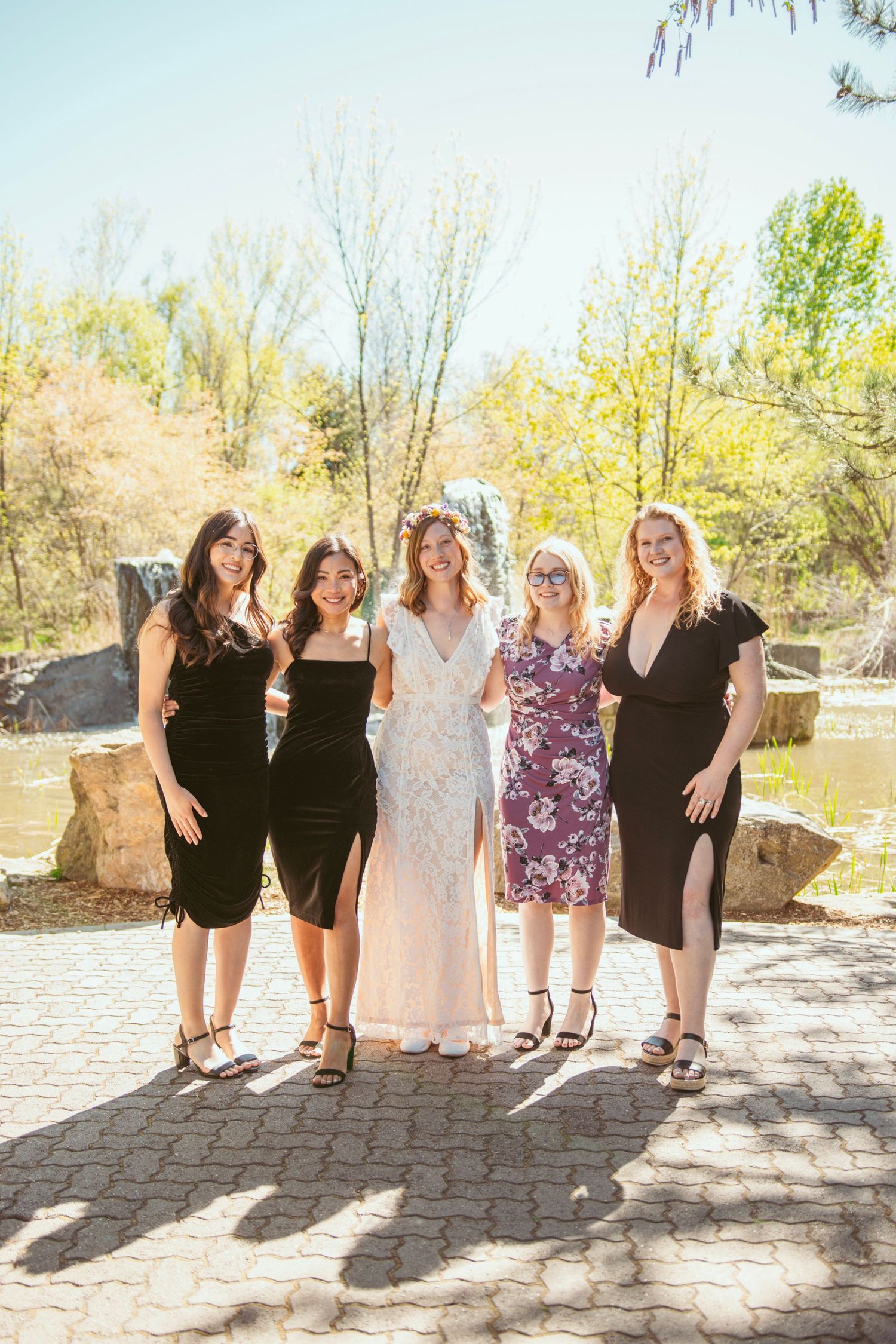 Bridesmaids in black dresses pose together on a sunny stone patio.
