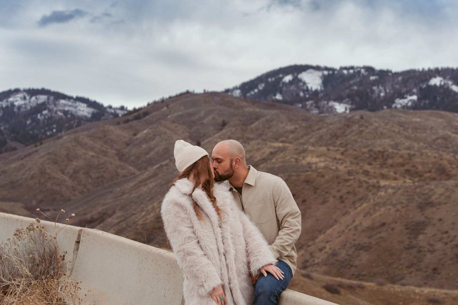 A couple embraces in front of snow-capped mountains during a winter engagement photoshoot.