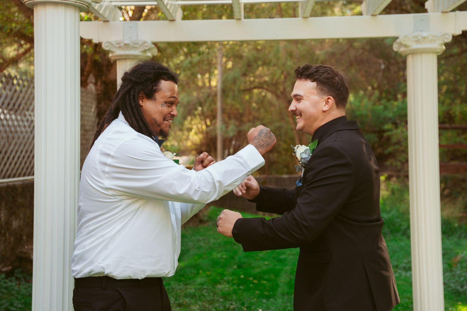 Wedding party members share playful poses under a white garden pergola.