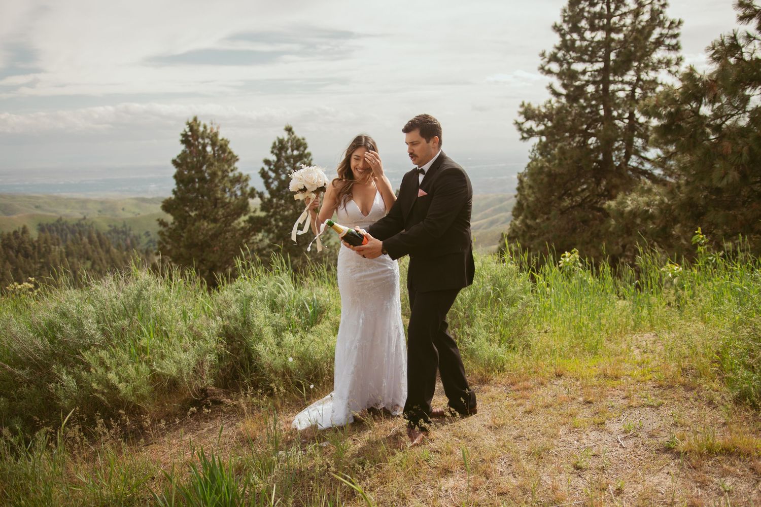 A bride and groom share an intimate moment on a hilltop with evergreen trees and mountain views.