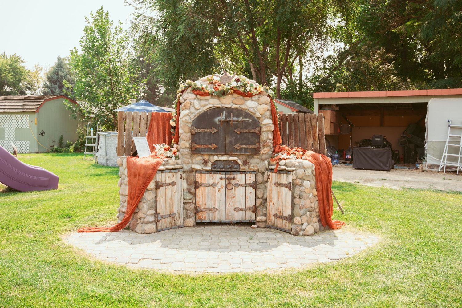 Stone outdoor fireplace and seating area surrounded by green lawn.