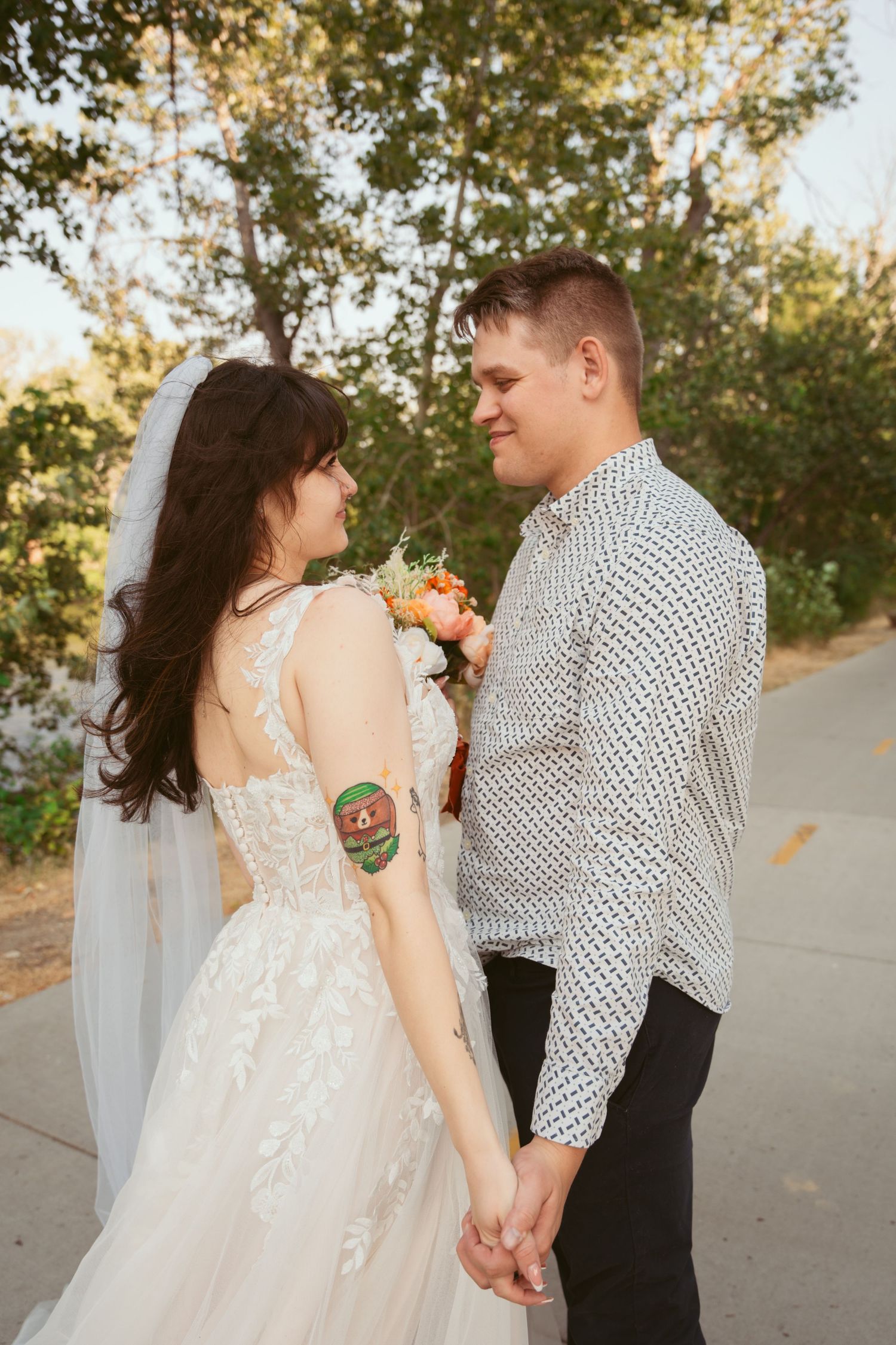 A romantic wedding couple shares an intimate moment outdoors with sunlit trees in the background.