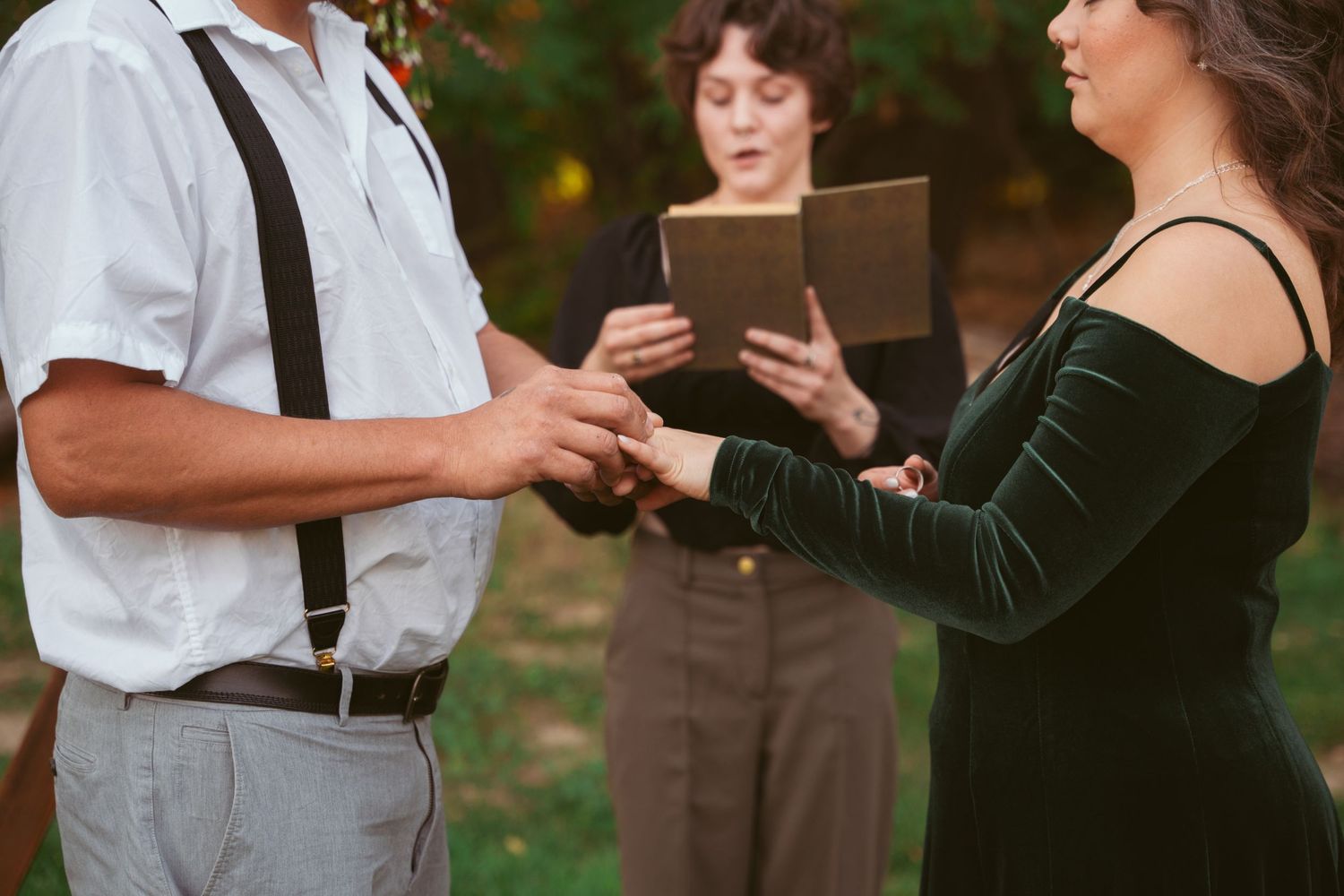 Close-up of hands exchanging wedding rings during an outdoor ceremony.