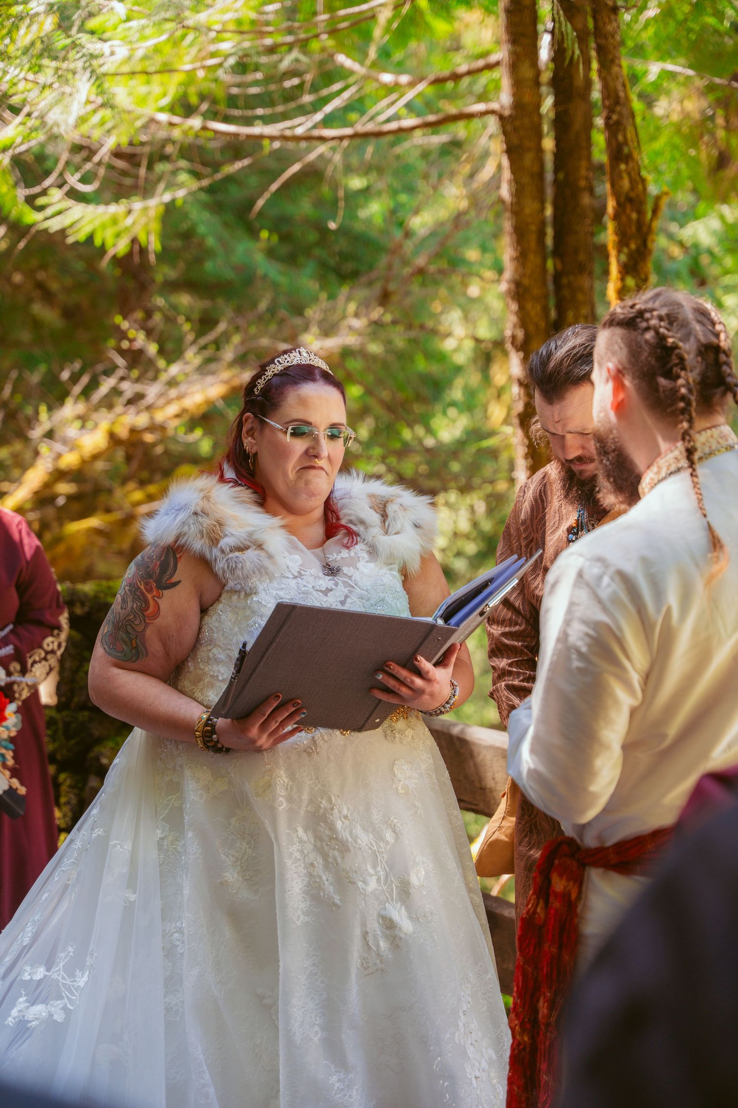 A wedding ceremony moment captured in a forest setting with attendees holding ceremony books.