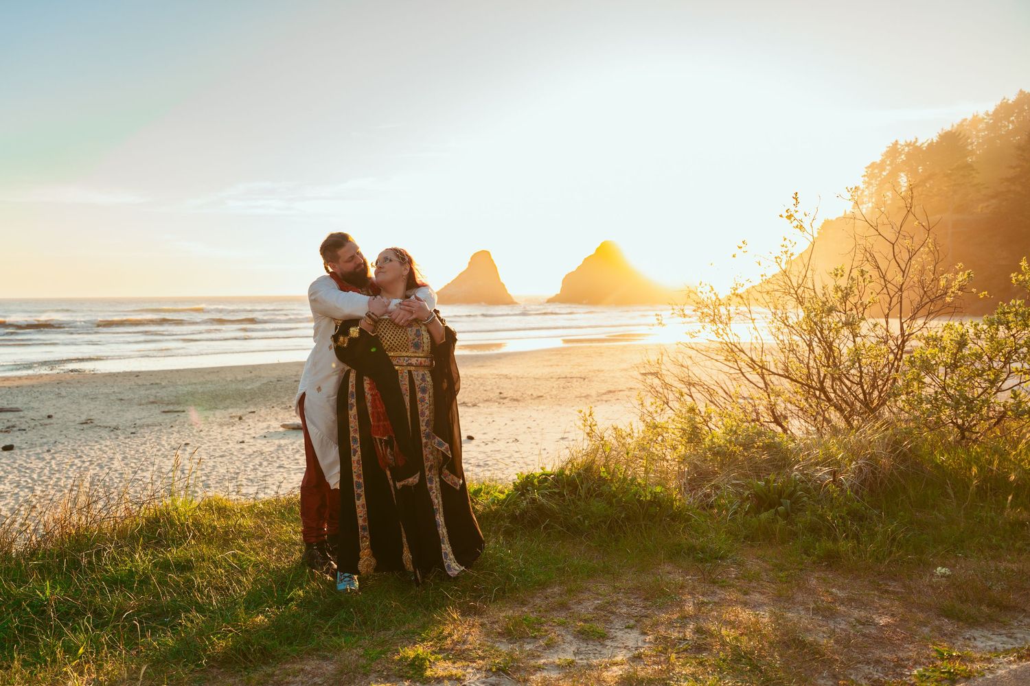A tender moment between two people on a grassy beach overlook during golden hour.