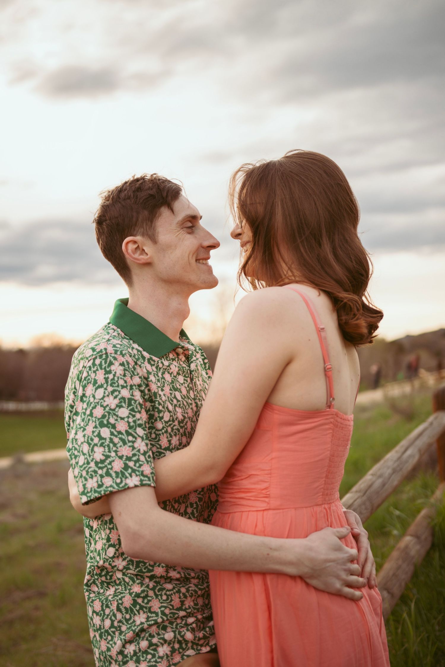 A couple embraces in a field during sunset, wearing spring outfits.