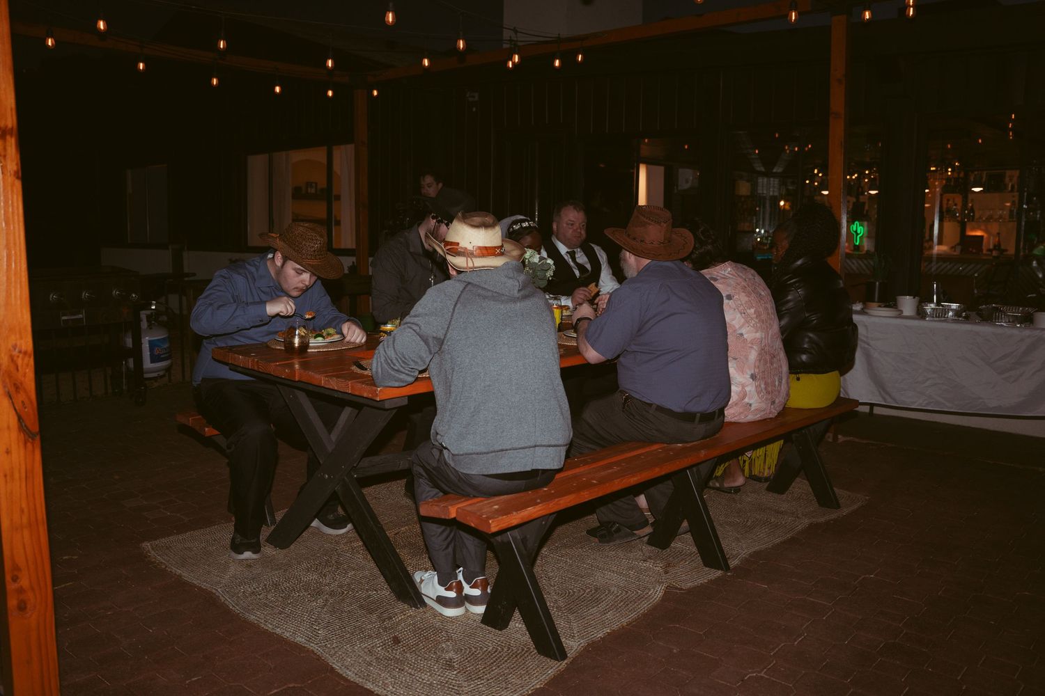 Evening wedding reception with string lights and wooden benches.