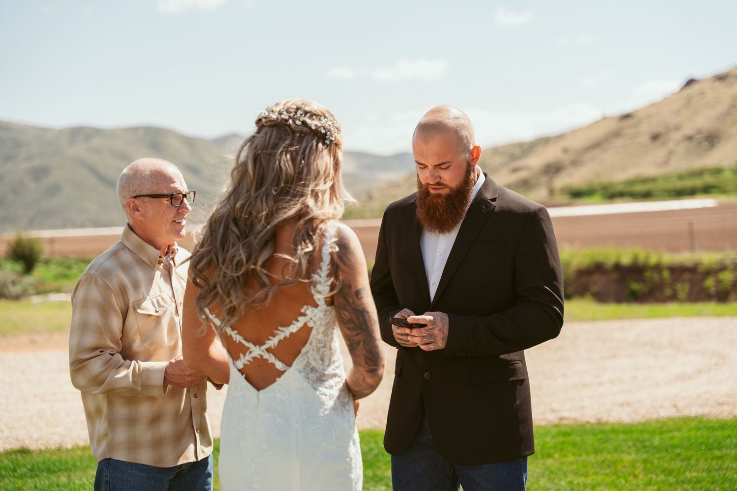 Outdoor wedding ceremony scene with guests seated on white chairs against a mountainous backdrop.