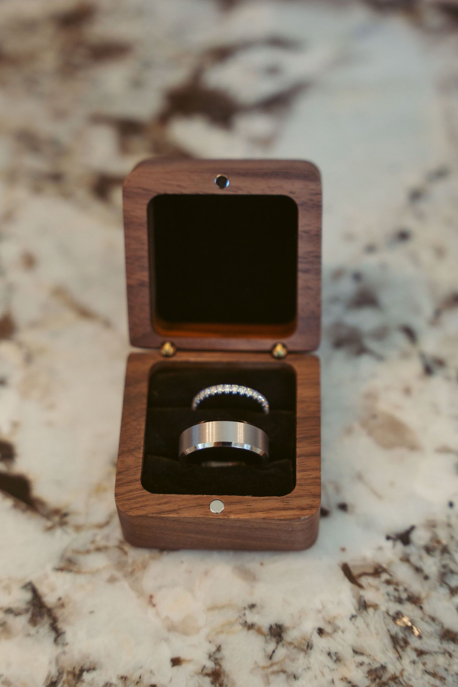 Close-up views of wedding bands in wooden ring boxes on marble surface.