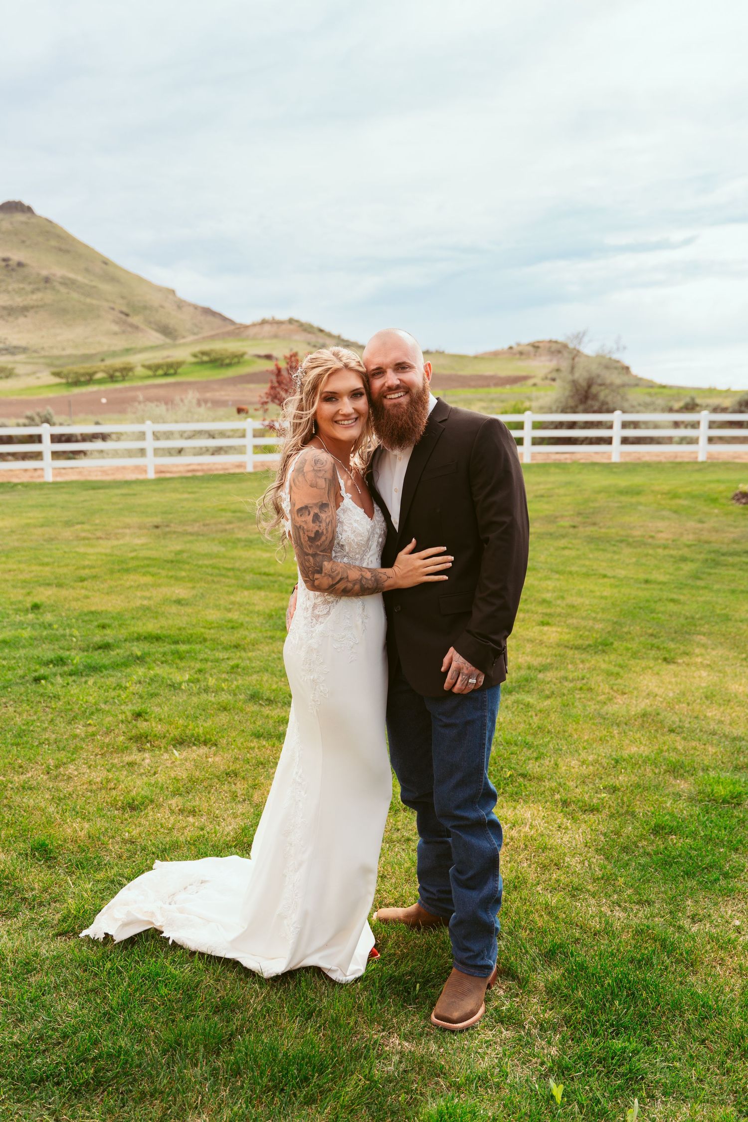 Wedding couple posing in front of mountain landscape with white fence.