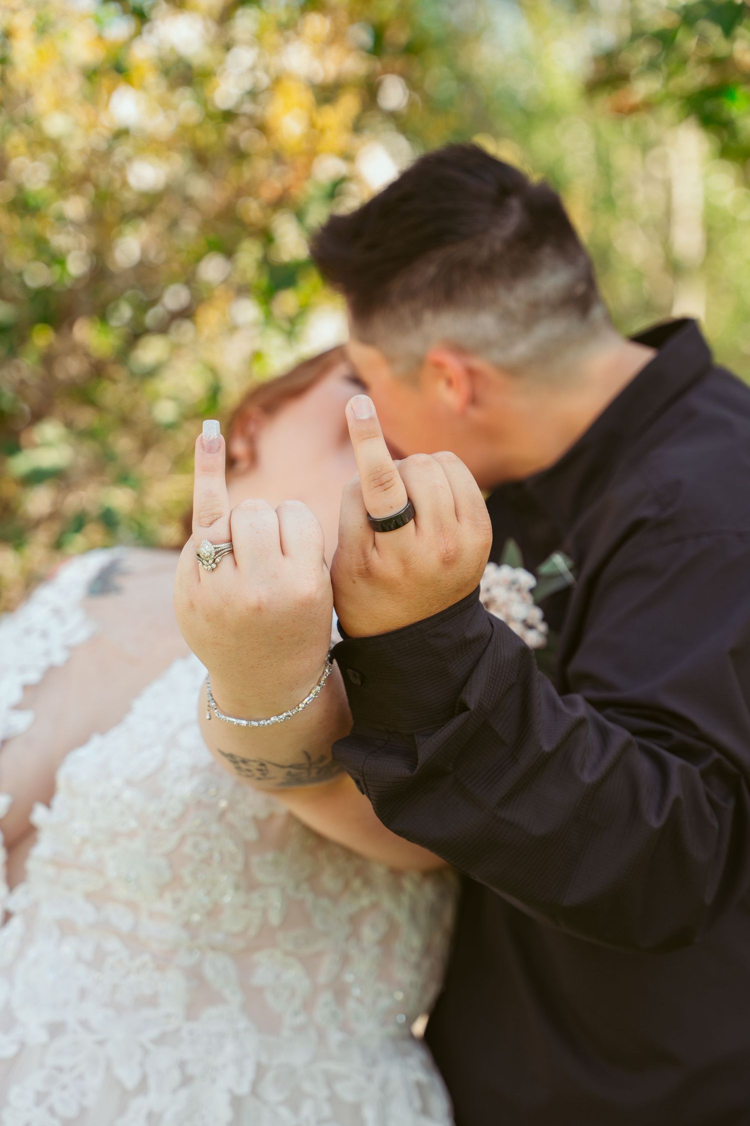 Close-up of newlyweds' hands showing wedding rings and bridal jewelry against a soft bokeh nature background.