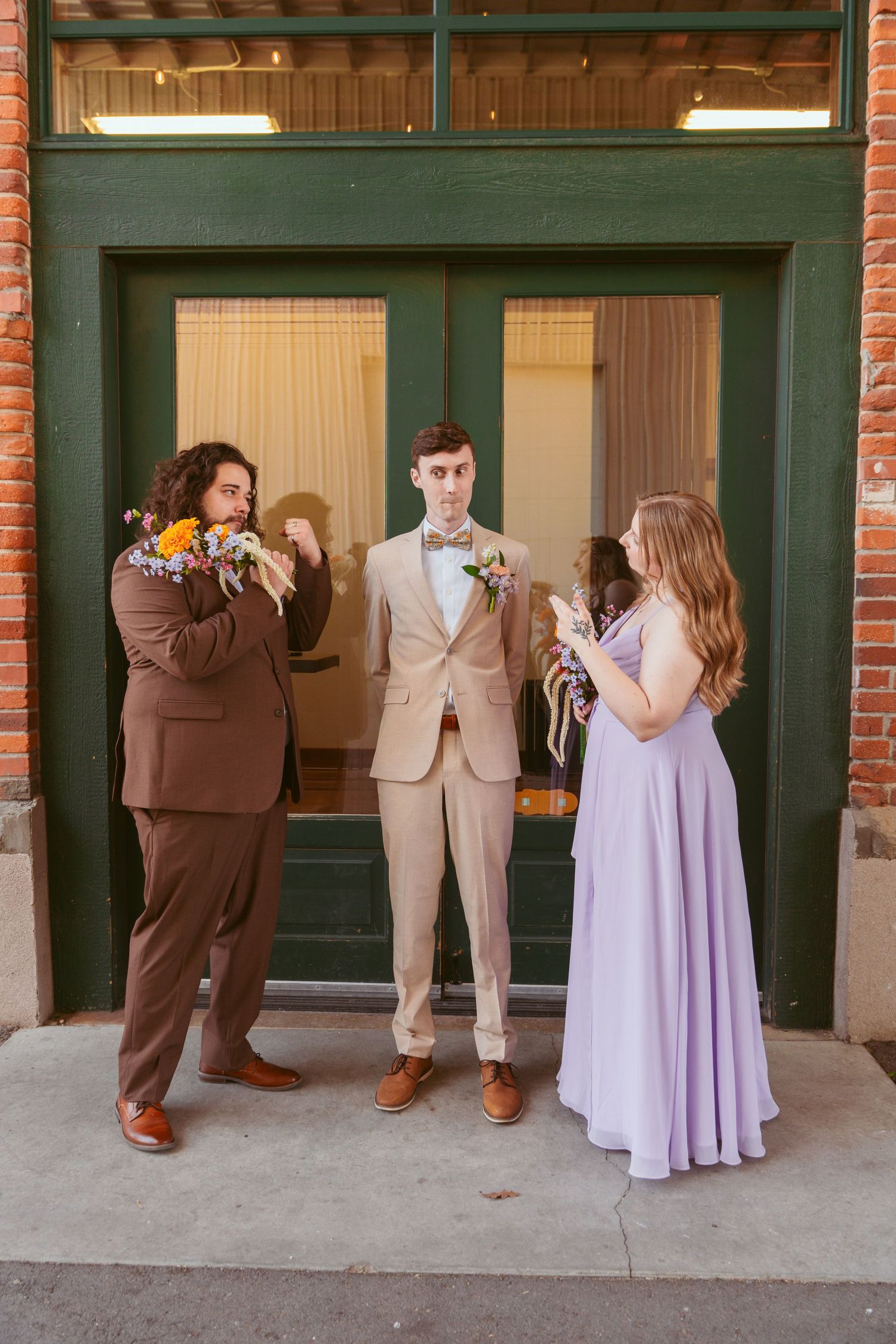 A candid wedding party moment showing playful interactions outside a brick building.